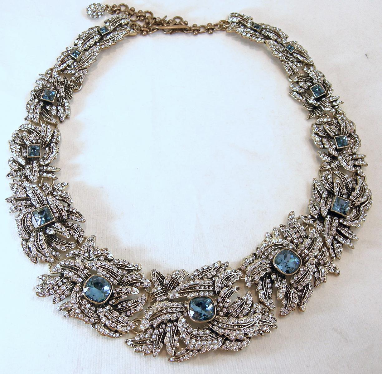 This vintage Heidi Daus necklace has a 3-dimensional design with clear crystals and accented with blue oval crystals in a gold tone setting. The necklace measures 23” x 1-3/4” with a hook clasp. It is signed “Heidi Daus” and is in excellent