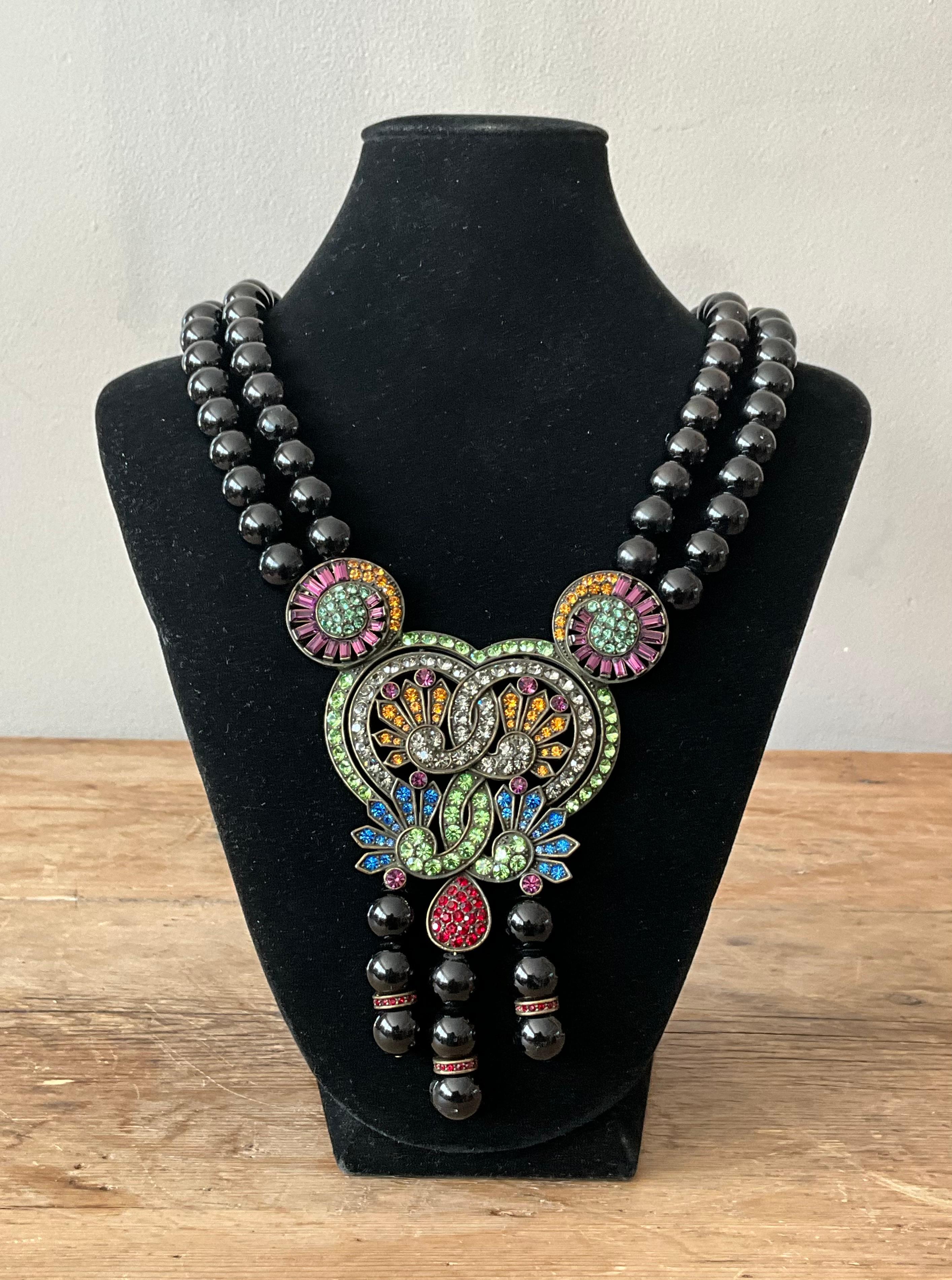 Questa collana vintage a doppio filo ispirata a Heidi Daus irradia un glamour opulento e vintage con un tocco audace e teatrale. Caratterizzata da due fili di perline di vetro riccamente colorate - spesso in tonalità Jewell come l'ambra profonda, lo