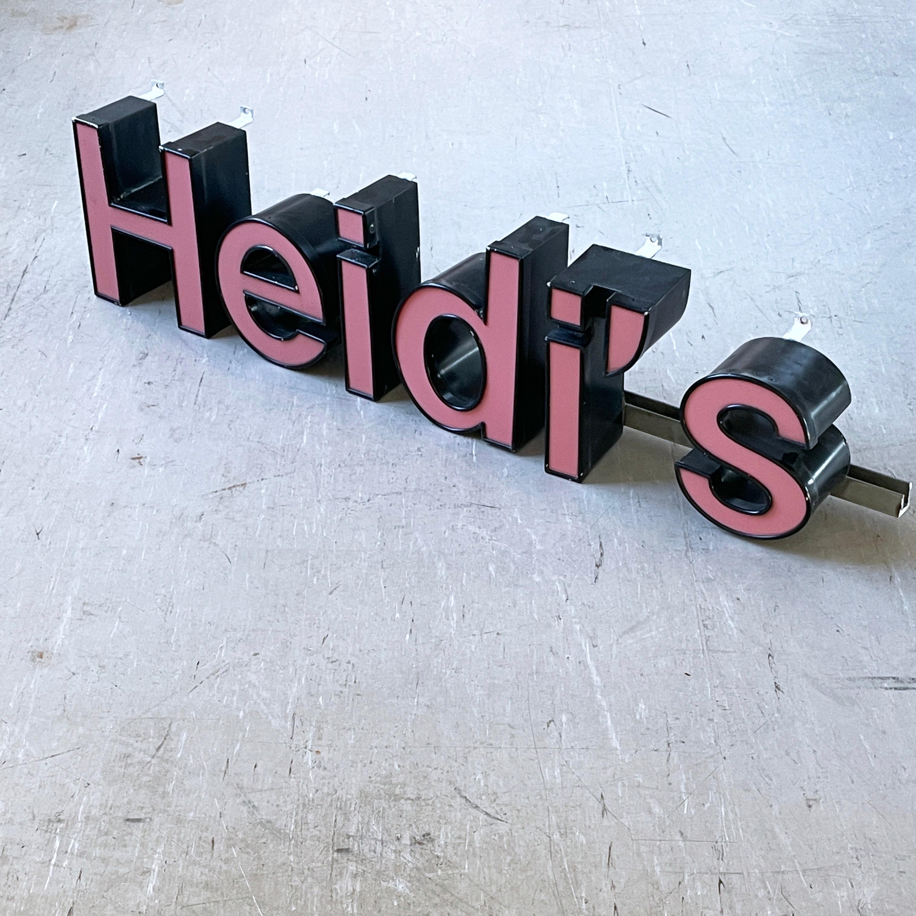 Rótulo de escaparate antiguo de Light Reclamation 'Heidi's'. Frontal acrílico rojo pálido con carcasa metálica. Montada en una varilla de acero con ganchos para colgar en la pared. Necesita recableado, ya que actualmente no tiene conexiones