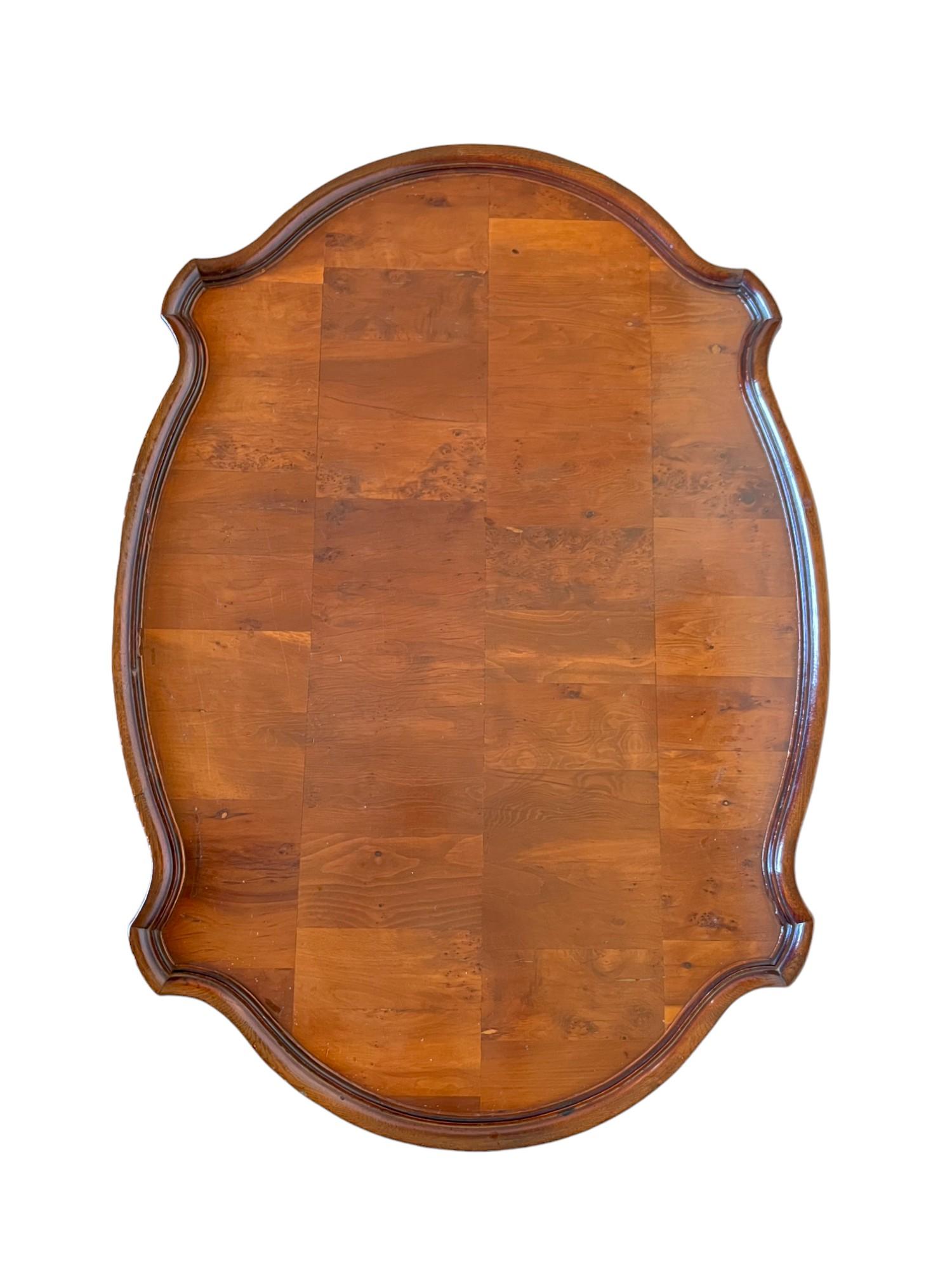 A vintage Hollywood Regency faux bamboo coffee or cocktail table by Hekman Furniture of the 1970's Bambu Regency collection. It features an oval patchwork burl wood top surface with a scalloped and beveled lipped edge, turned wood saber style