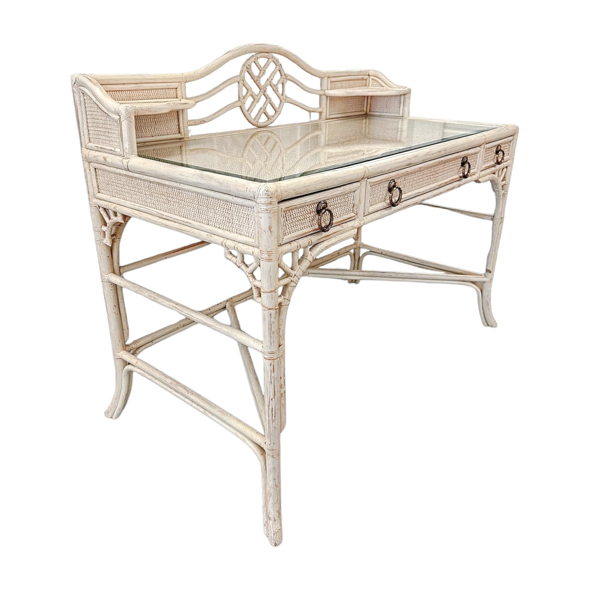 This vintage Hekman rattan desk combines elegance and functionality with its intricate fretwork design and airy coastal aesthetic. The natural rattan frame is finished in a light, washed white tone, giving it a versatile presence that suits both