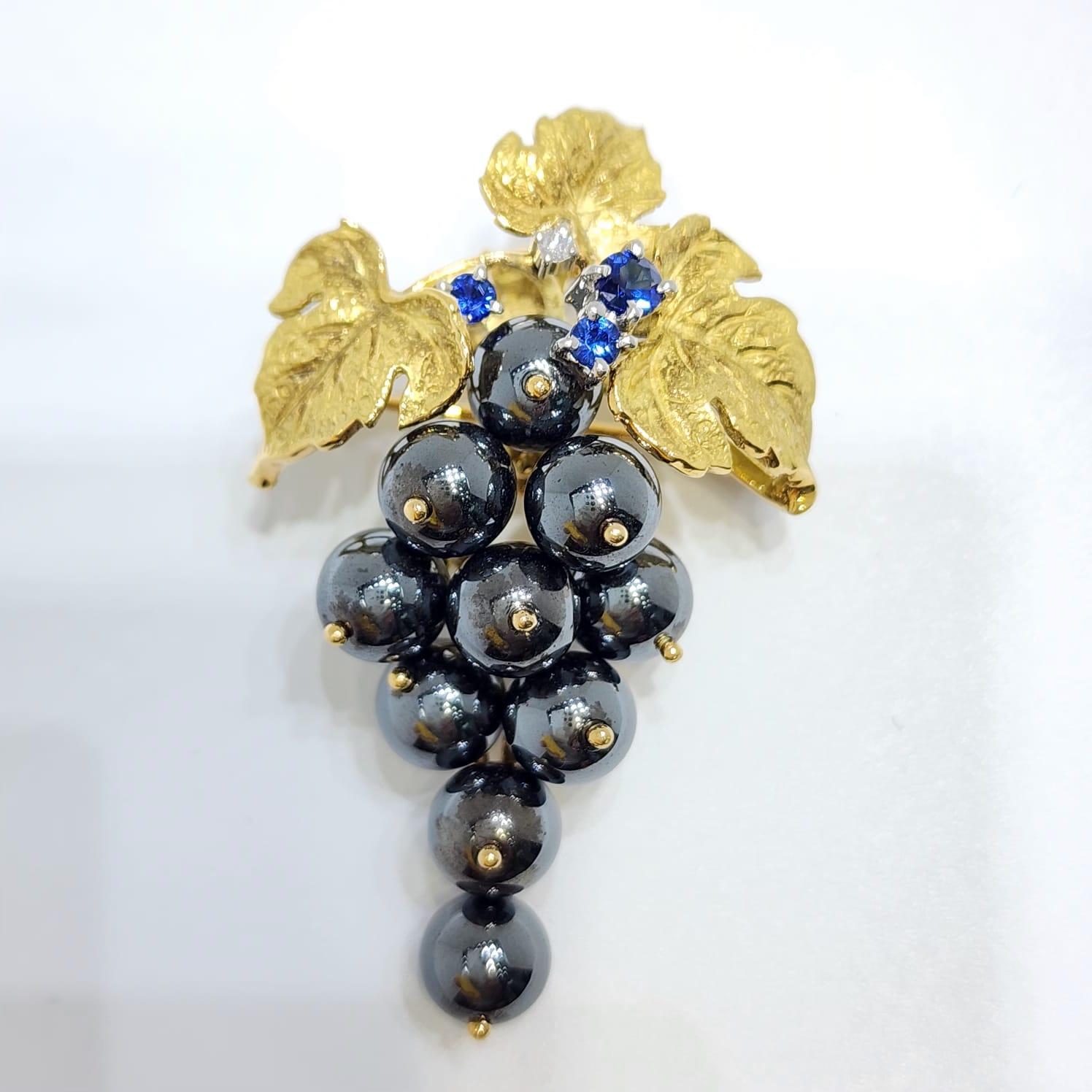 Questa spilla e ciondolo vintage, un'affascinante miscela di estrosità ed eleganza, presenta un design a grappolo d'uva splendidamente scolpito e realizzato in lussuoso oro giallo 18 carati. Le perle di ematite lucida formano i grappoli d'uva,