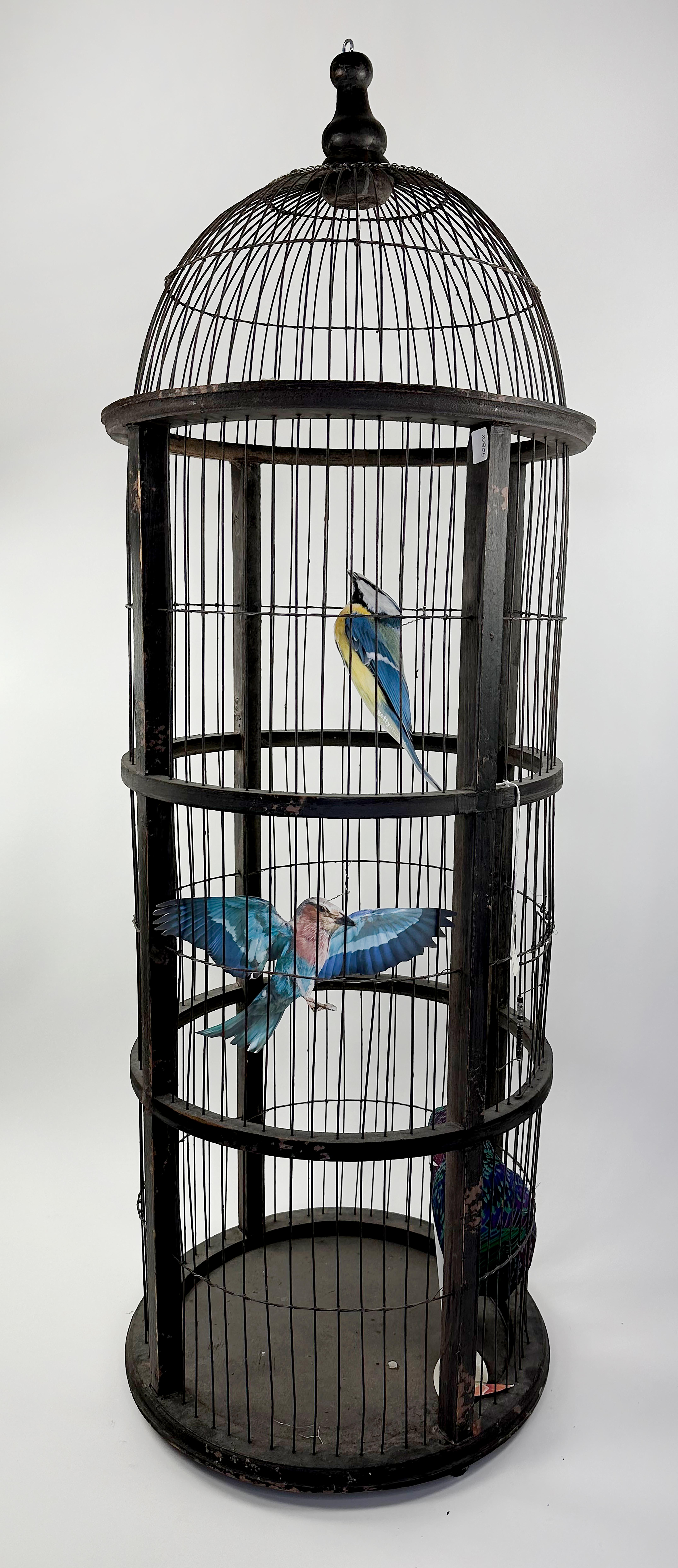 Une cage à oiseaux ronde en bois vintage, rustique et haute, fabriquée à la main, dans une finition originale. Un câblage en acier est utilisé pour créer une enceinte. Une petite porte s'ouvre sur la cage dans la partie inférieure ou moyenne de