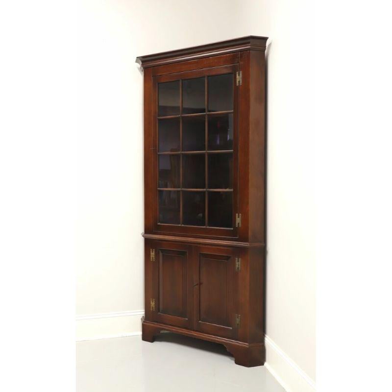 A corner display cabinet in solid Mahogany by Henkel Harris. Made in Winchester, Virginia, USA, circa 1950's. Chippendale style with bracket feet and brass hardware. Upper cupboard features three fixed wooden shelves with plate grooves behind a