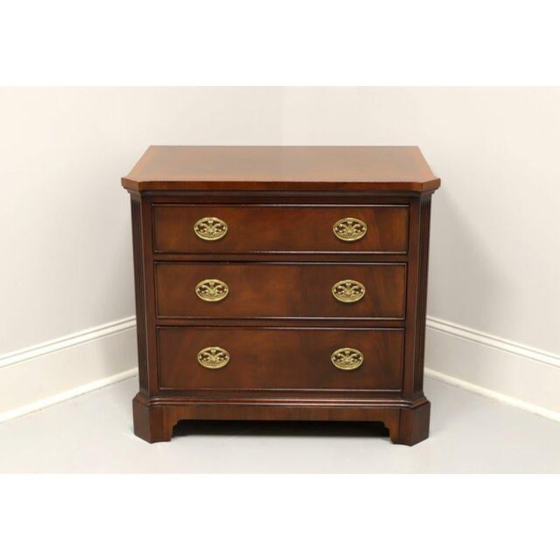 A Hepplewhite style nightstand by Henkel Harris of Winchester, Virginia, USA. Mahogany with brass hardware, banded top, fluted columns and bracket feet. Features three drawers of dovetail construction, with top drawer having a concealed, slide back,