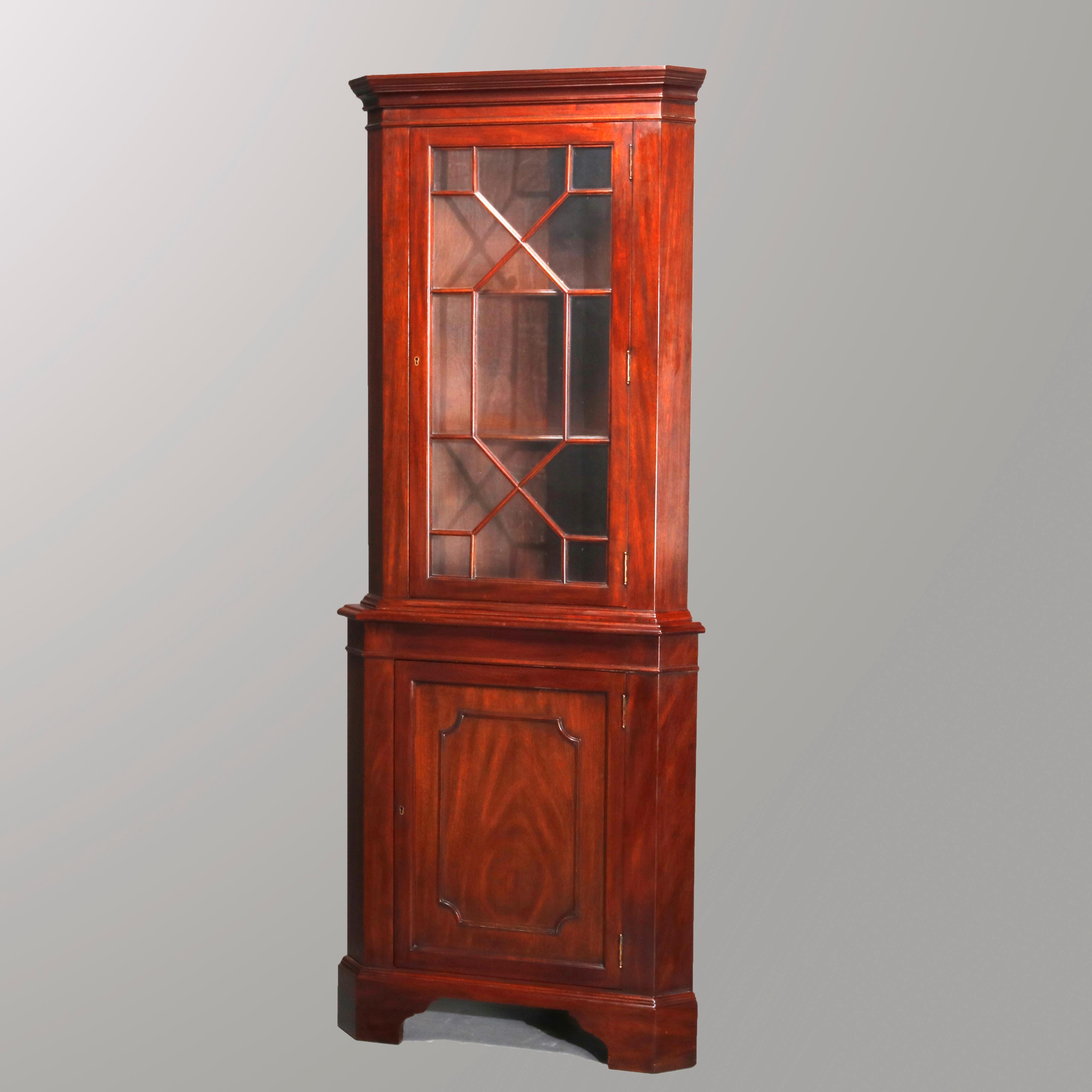 A vintage Georgian style corner cupboard by Henkel Harris for Virginia Galleries offers mahogany construction with upper mullioned door opening to shelved interior and seated on base with paneled single door cabinet, raised on bracket feet, labels