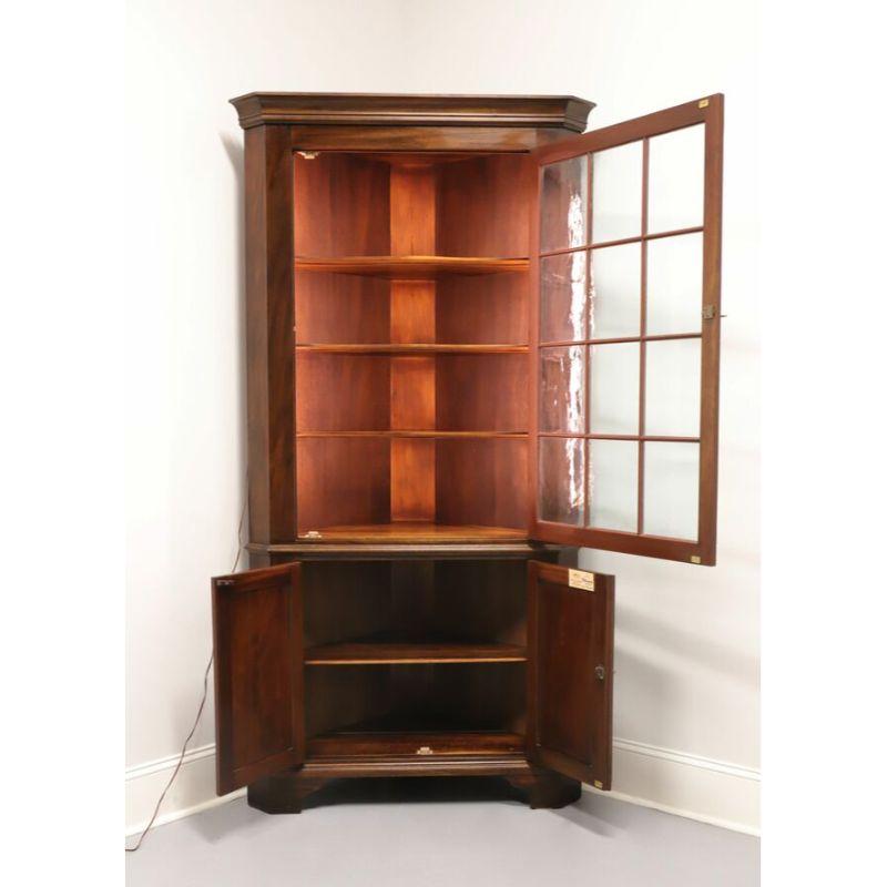 A corner cupboard in solid Mahogany by Henkel Harris. Made in Winchester, Virginia, USA in 1971. Chippendale style with bracket feet and brass hardware. Upper lighted cupboard features three fixed wooden shelves with plate grooves behind a lockable