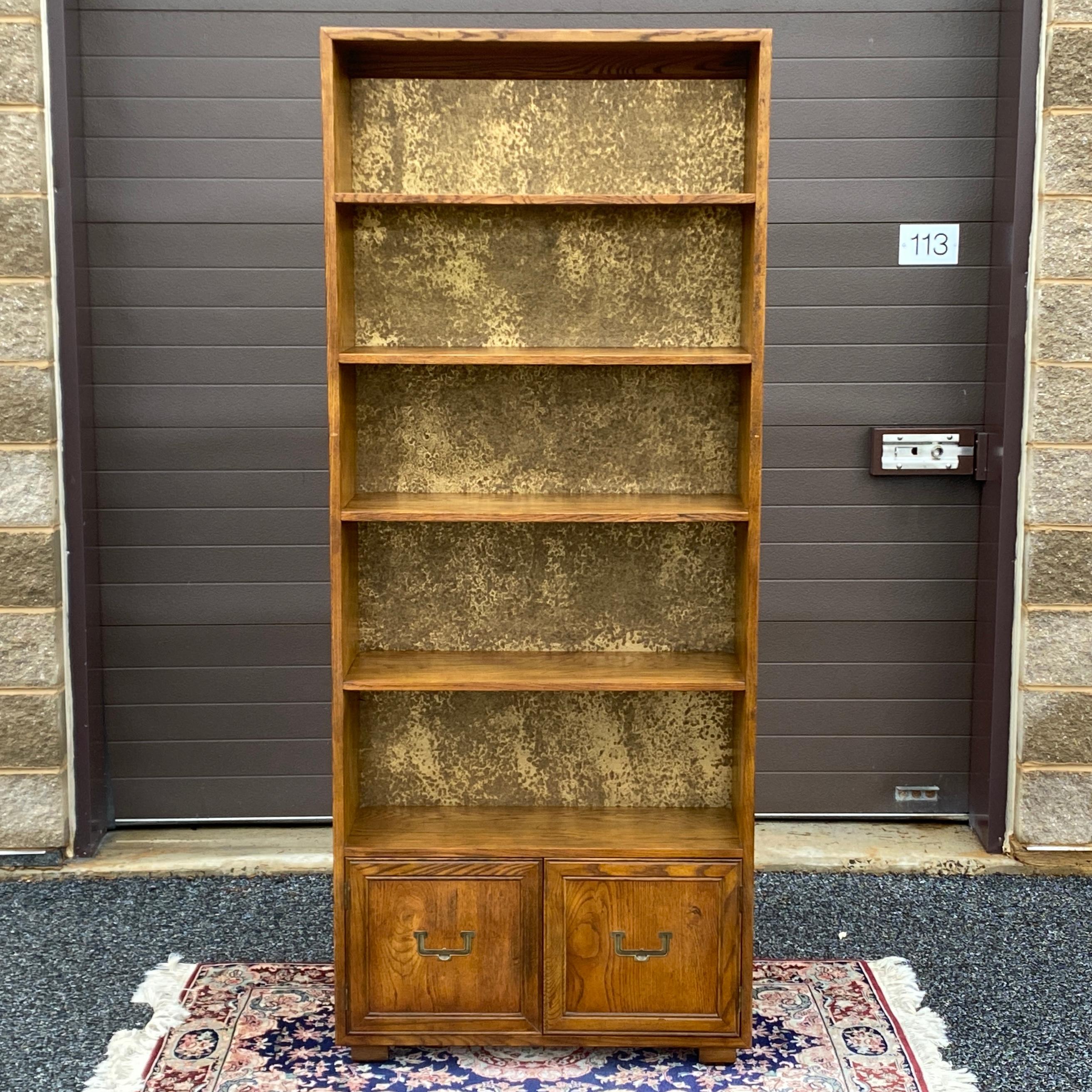 A rare bookcase from the Artefacts collection by Henredon featuring five shelves with decorative brass back panel over cabinet space with the iconic flush campaign style door hardware.

Fixed shelf height measurements from the top