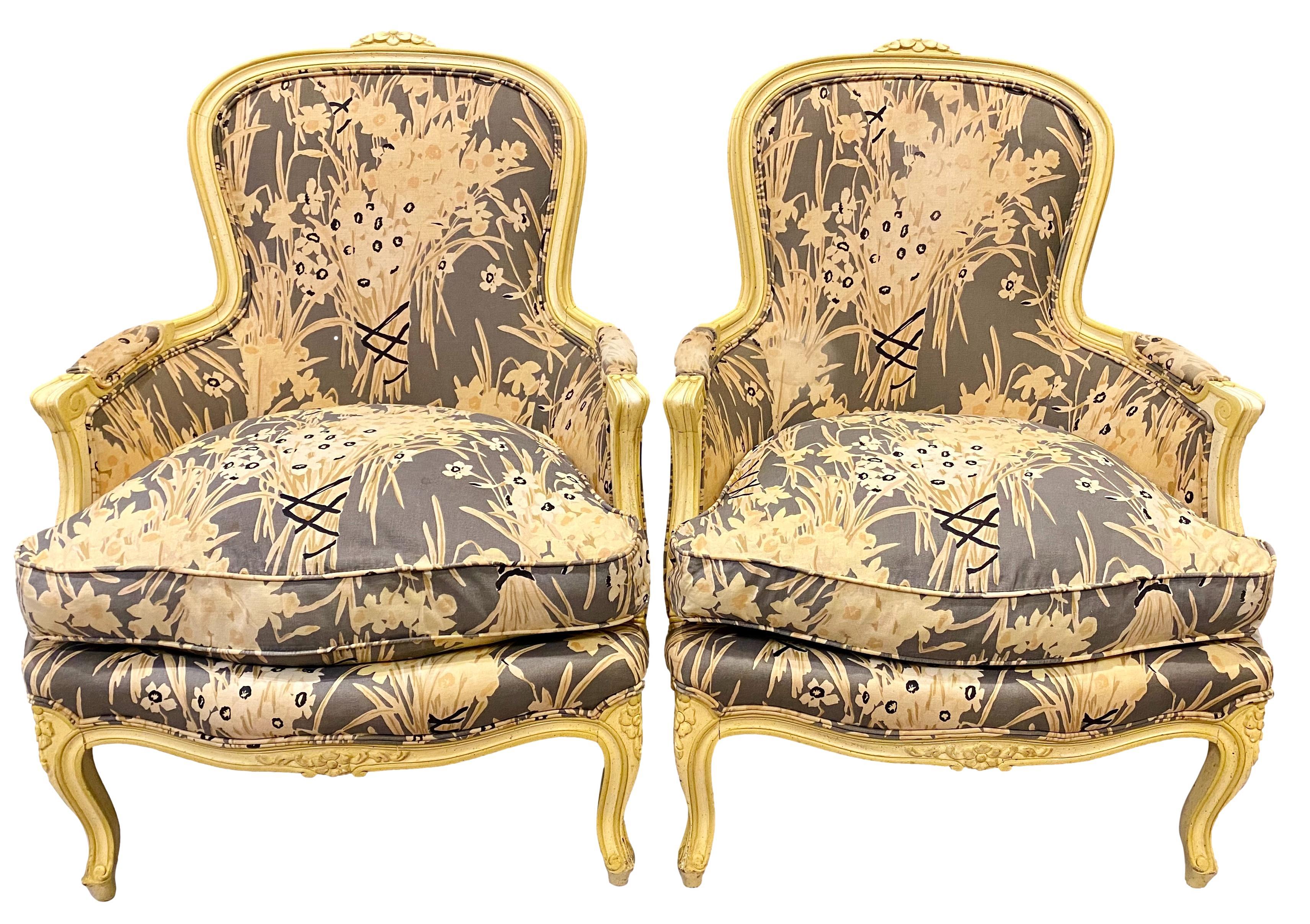 A late 1970s pair of French Louis XV style bergère chairs by Henredon. Carved and channeled wood frames with tonal cream finish. Cotton canvas upholstery fabric in beige-gray, tan, cream & gold with black accents. Down filled seat