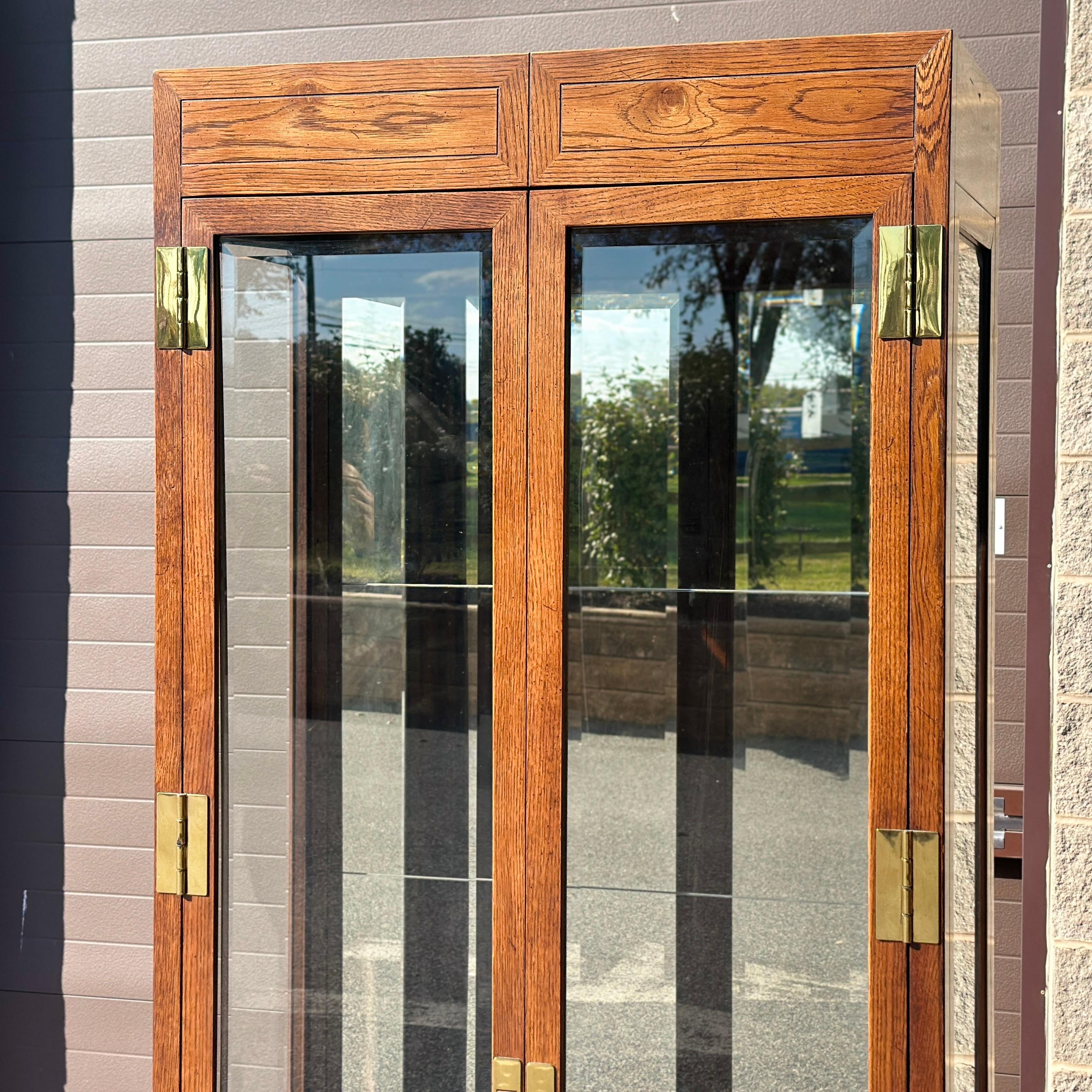 A sparkling campaign style Henredon campaign style display cabinet from their iconic Scene One Collection. Two full length doors with beveled glass open to a mirrored back interior with 4 thick glass adjustable shelves with plate grooves. The