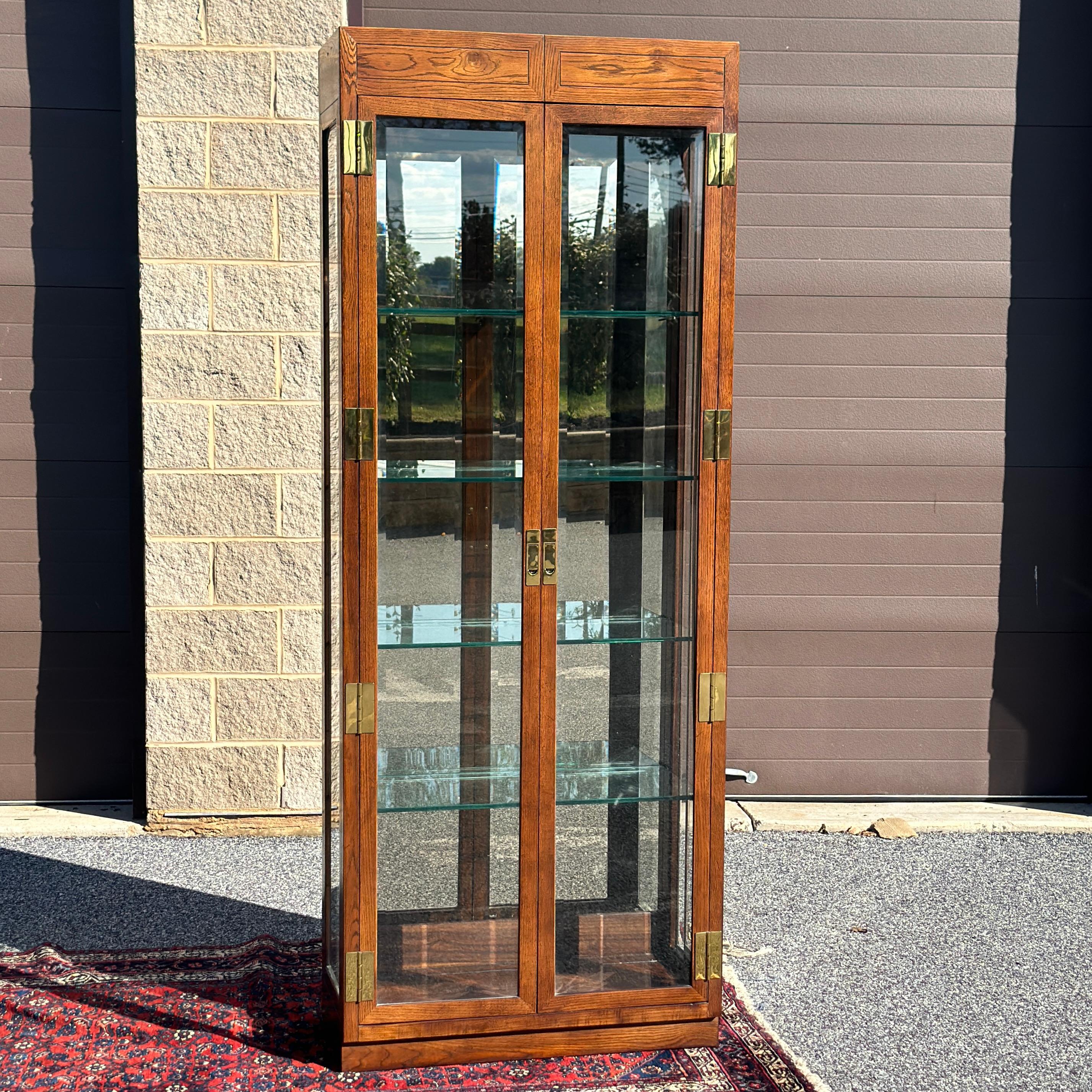 A sparkling campaign style Henredon campaign style display cabinet from their iconic Scene One Collection. Two full length doors with beveled glass open to a mirrored back interior with 4 thick glass adjustable shelves with plate grooves. The