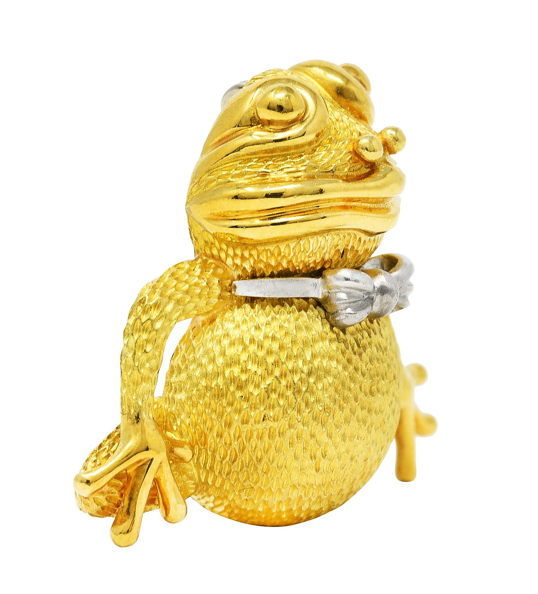 Brooch designed as a cartoonish squatting frog with texture throughout

Featuring a platinum bow tie

Accented with high polished features

Completed by hinged pin stem with locking closure

Stamped 18k and PT950 for 18 karat gold and platinum,
