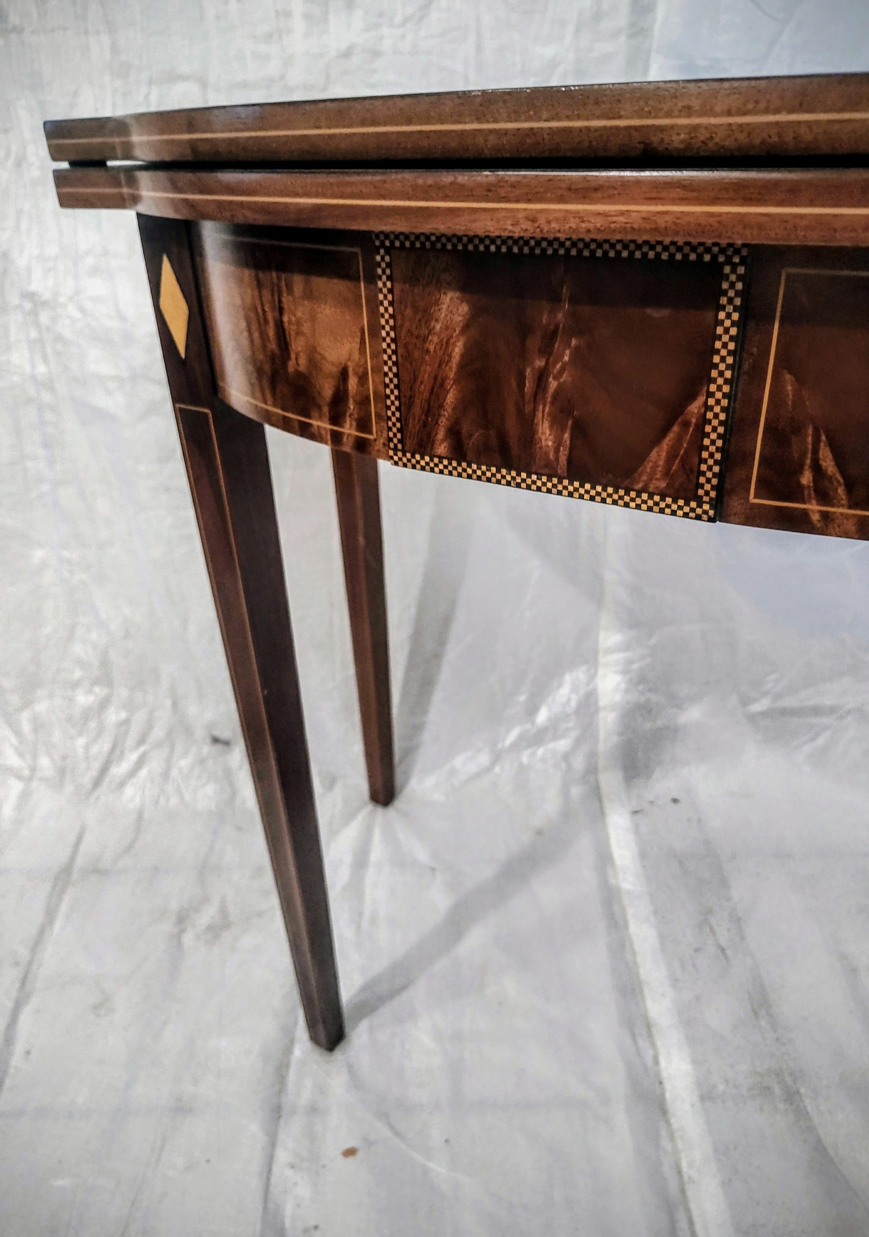 Vintage Hepplewhite Style Serpentine Shaped Mahogany Game Table. The table features crotch mahogany panels along the skirt board which are outlined with string inlays as are the legs. The raised center panel also in crotch mahogany is highlighted