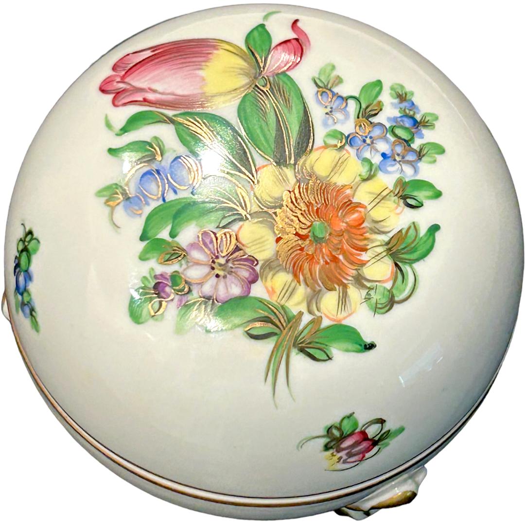 This vintage Herend porcelain floral trinket jewelry box is a true collector’s item.  Its hand-painted design depicts a beautiful floral design, making it a unique addition to any collection.  The round box, accented in gold trim, is made of
