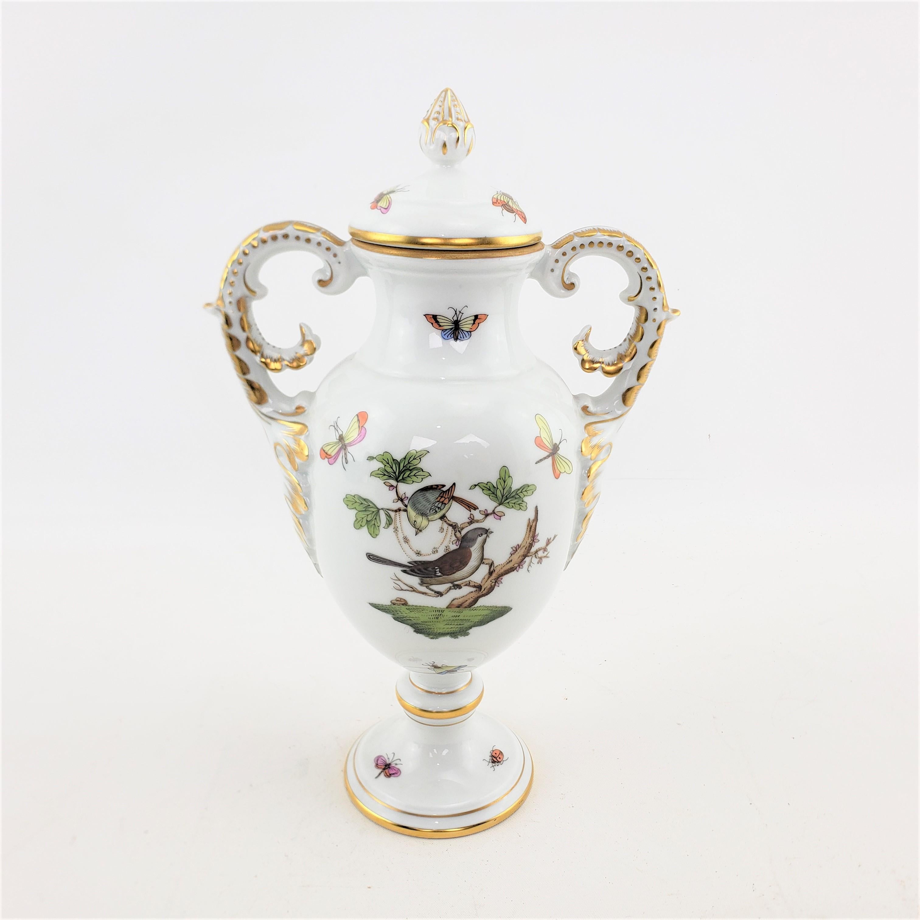 This lidded porcelain vase was made by the renowned Herend Pottery factory of Hungary in approximately 1970 in a Victorian style. The vase is done in the 'Rothschild Bird' pattern and has two different hand-painted bird panels, one on either side,