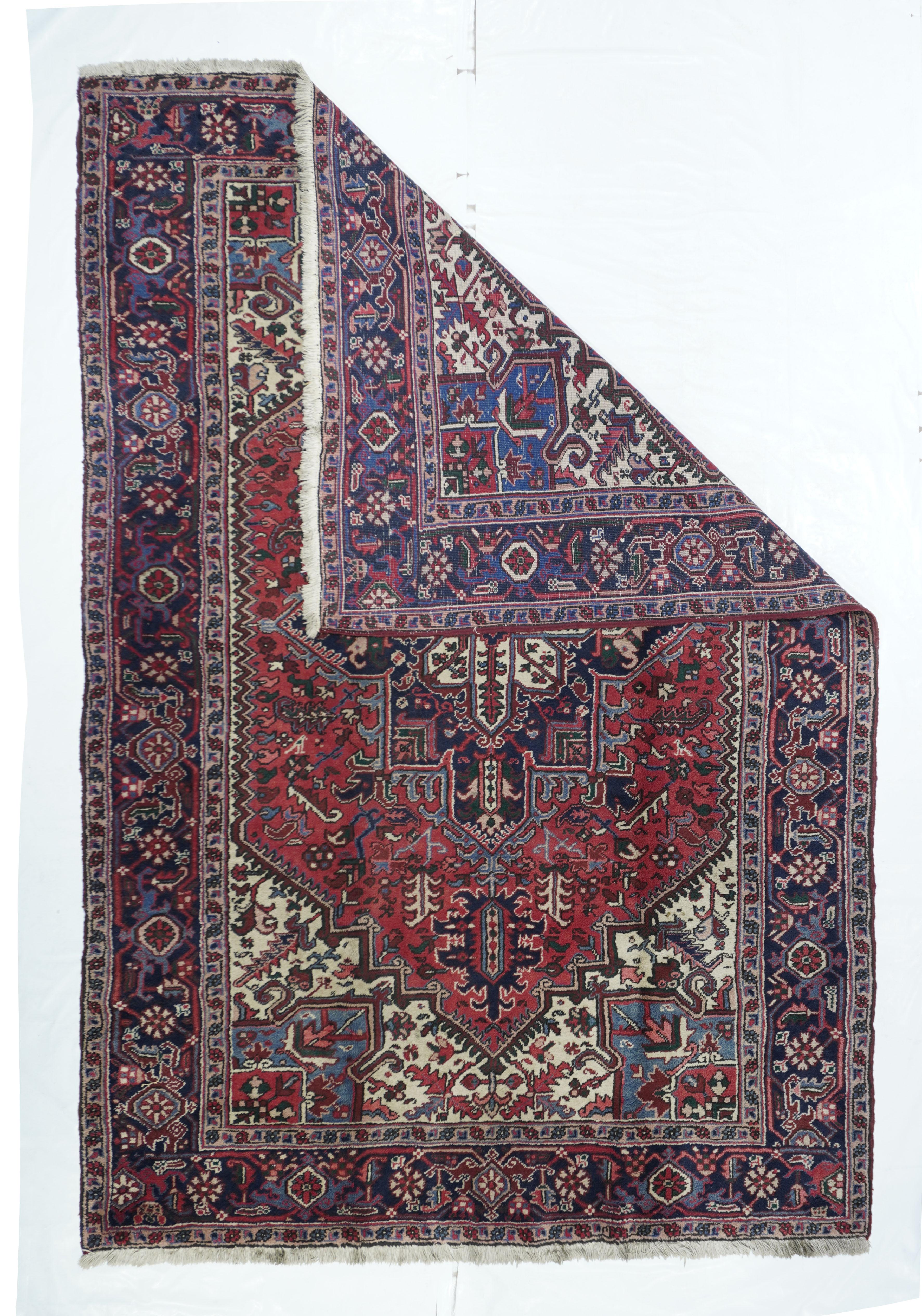 Vintage Heriz rug 6'7'' x 9'8''. The field is really ecru and it sneaks up along the zig-zag sides of the coral red subfield and expands into corners with serrated, oblique leaves around the blue projecting, pointed cores. Navy stepped medallion