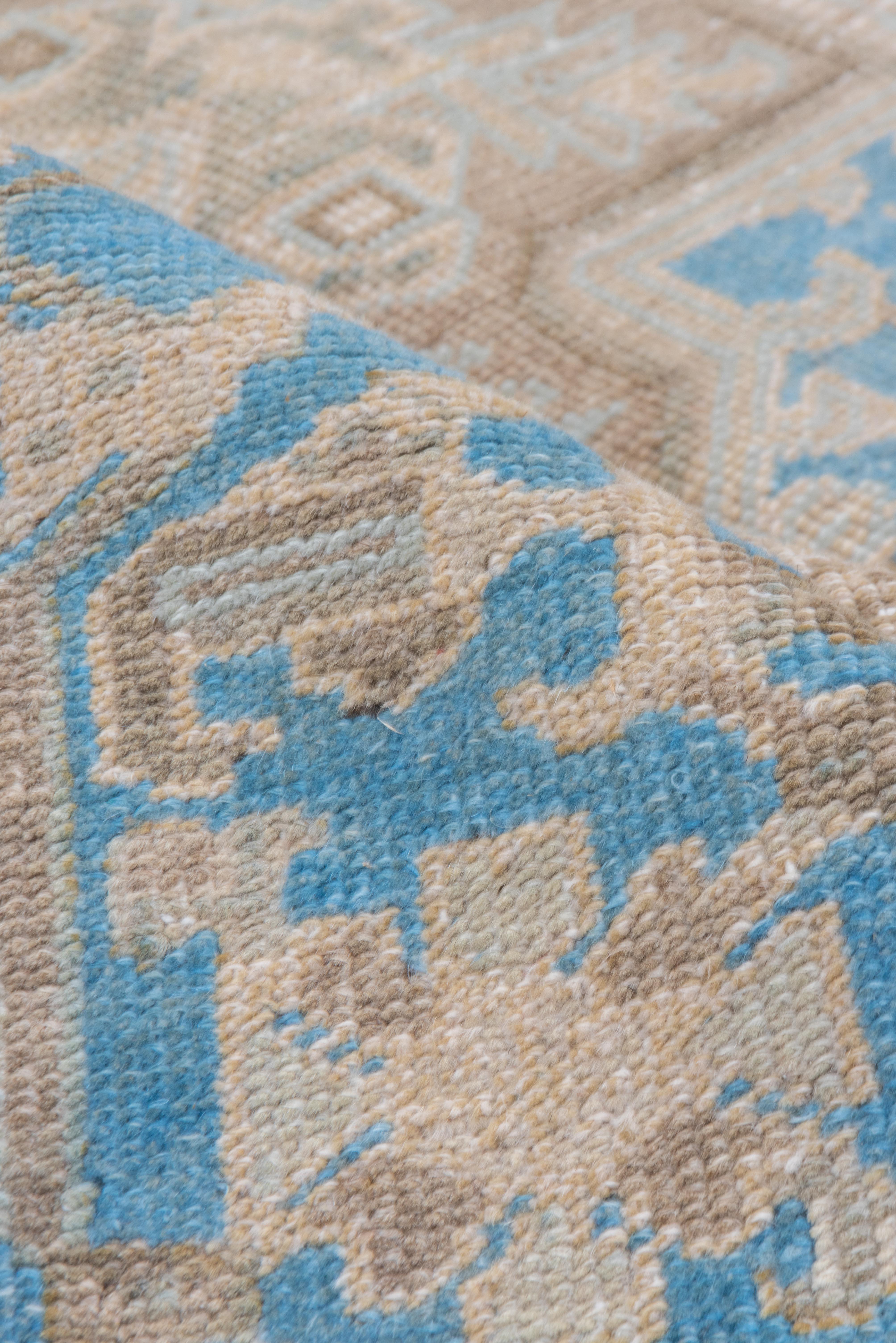 Ce tapis Heriz vintage présente un médaillon imposant sur un champ doux et délavé de gris cendré et de beige parcheminé, ponctué d'accents de bleu poudré qui ajoutent une touche délicate à la composition. Le motif central est anguleux et