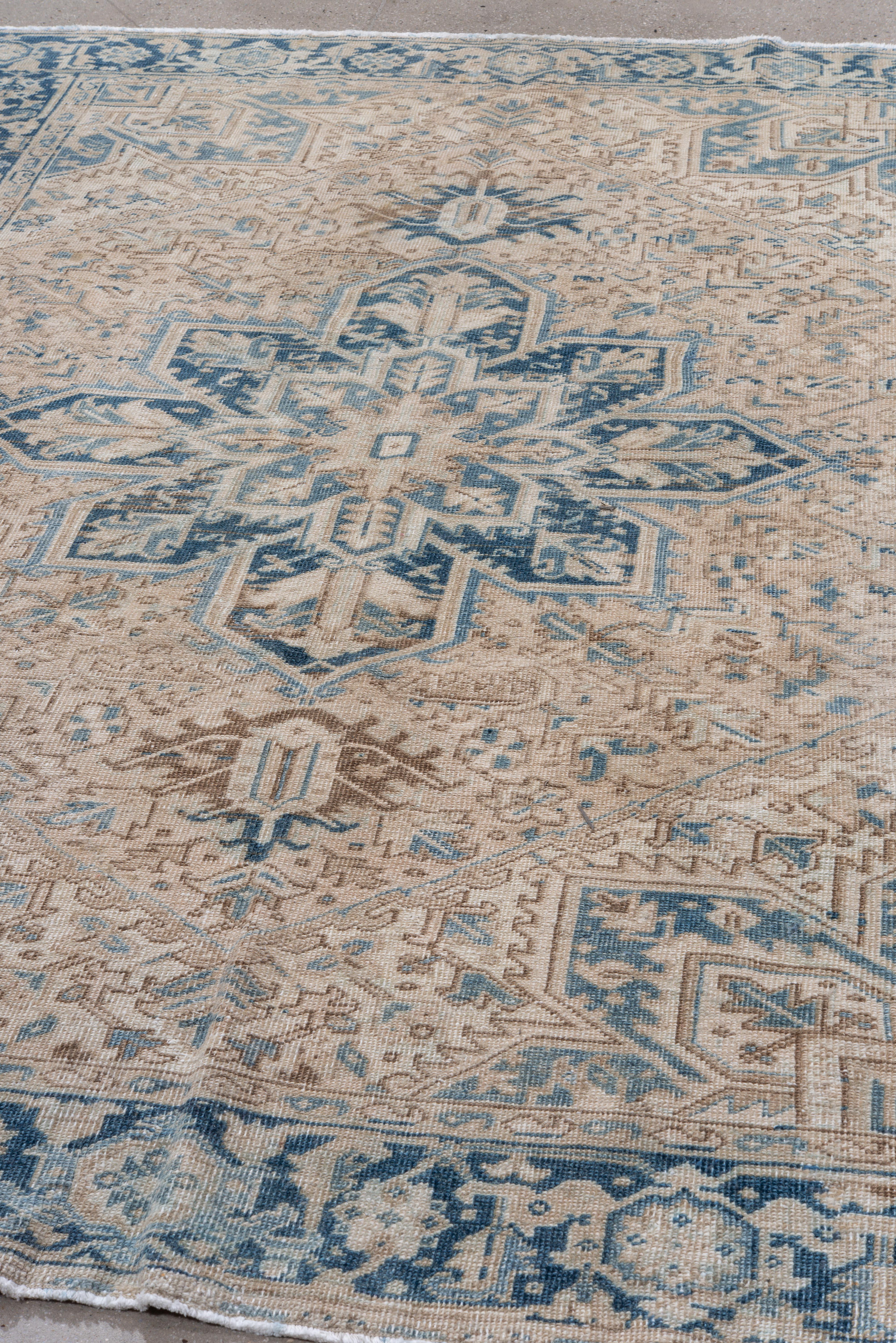 Questo tappeto vintage Heriz è caratterizzato da un grande medaglione centrale a raggiera nei toni stratificati dell'indaco, dell'ardesia e del blu ghiacciaio, su un campo di colore crema leggermente attenuato. Delicati accenti in sabbia, moka e
