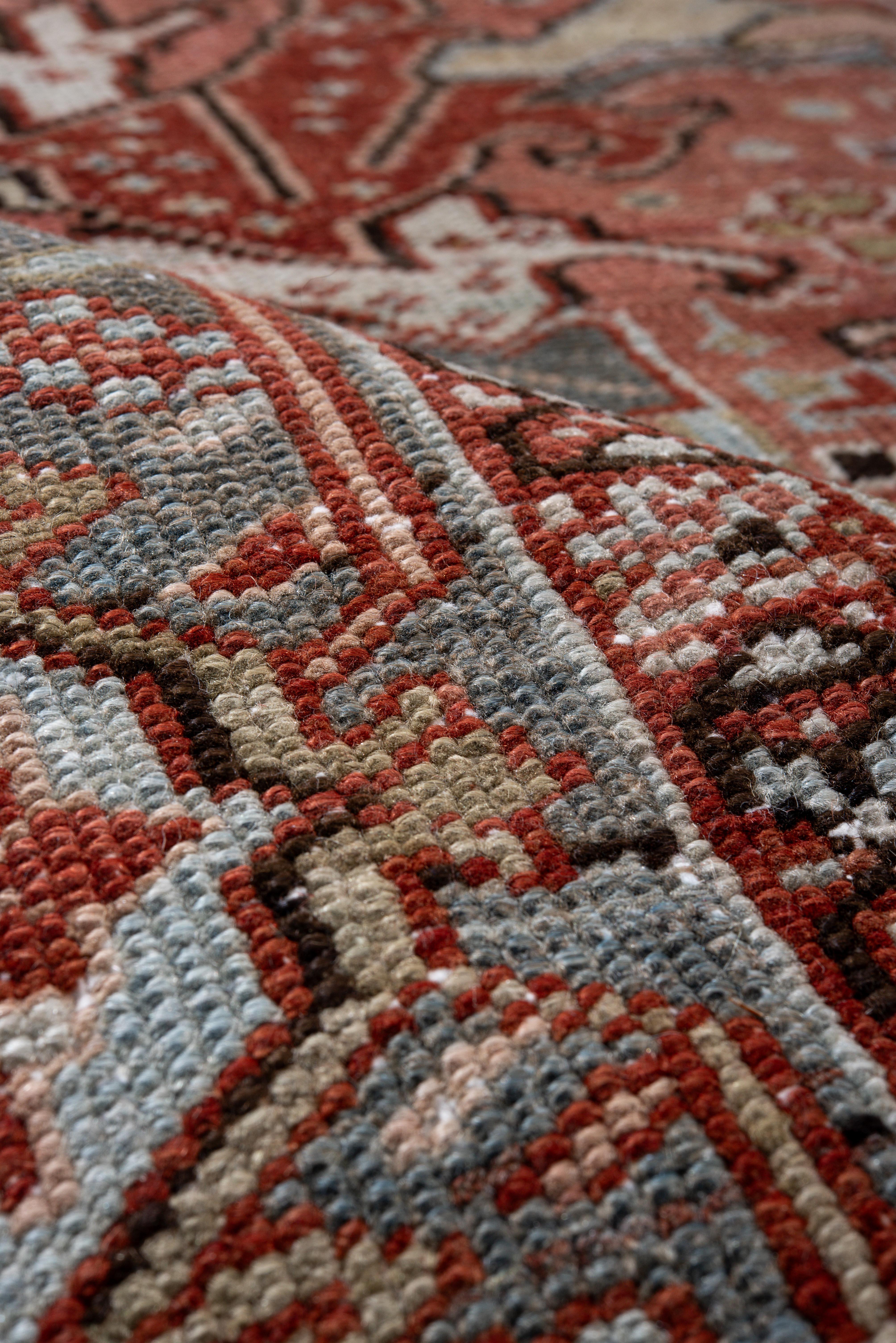 Esta alfombra Heriz vintage presenta un campo de terracota bellamente desgastado, animado por motivos botánicos angulosos y flores tribales en colores salvia apagado, índigo pálido y marfil tiza. El diseño central se organiza simétricamente en torno