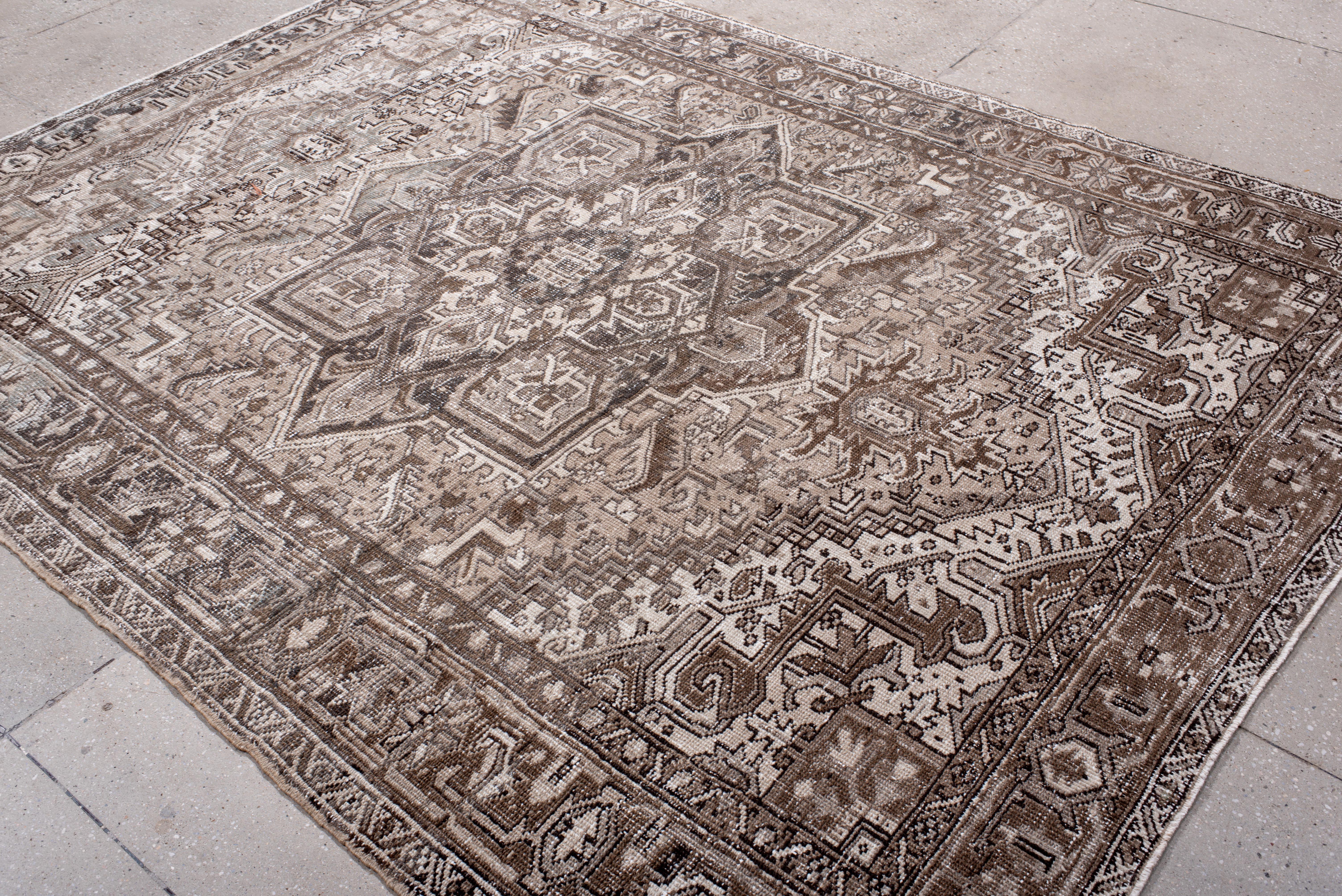 Auf elfenbeinfarbenem Grund mit taupefarbenen und taubengrauen Akzenten, umrahmt von einer warmen, sepiafarbenen Schutzbordüre, zeigt dieses Vintage Heriz ein eindrucksvolles Stufenmedaillon, das von stilisierten, eckigen Palmetten und geometrischen