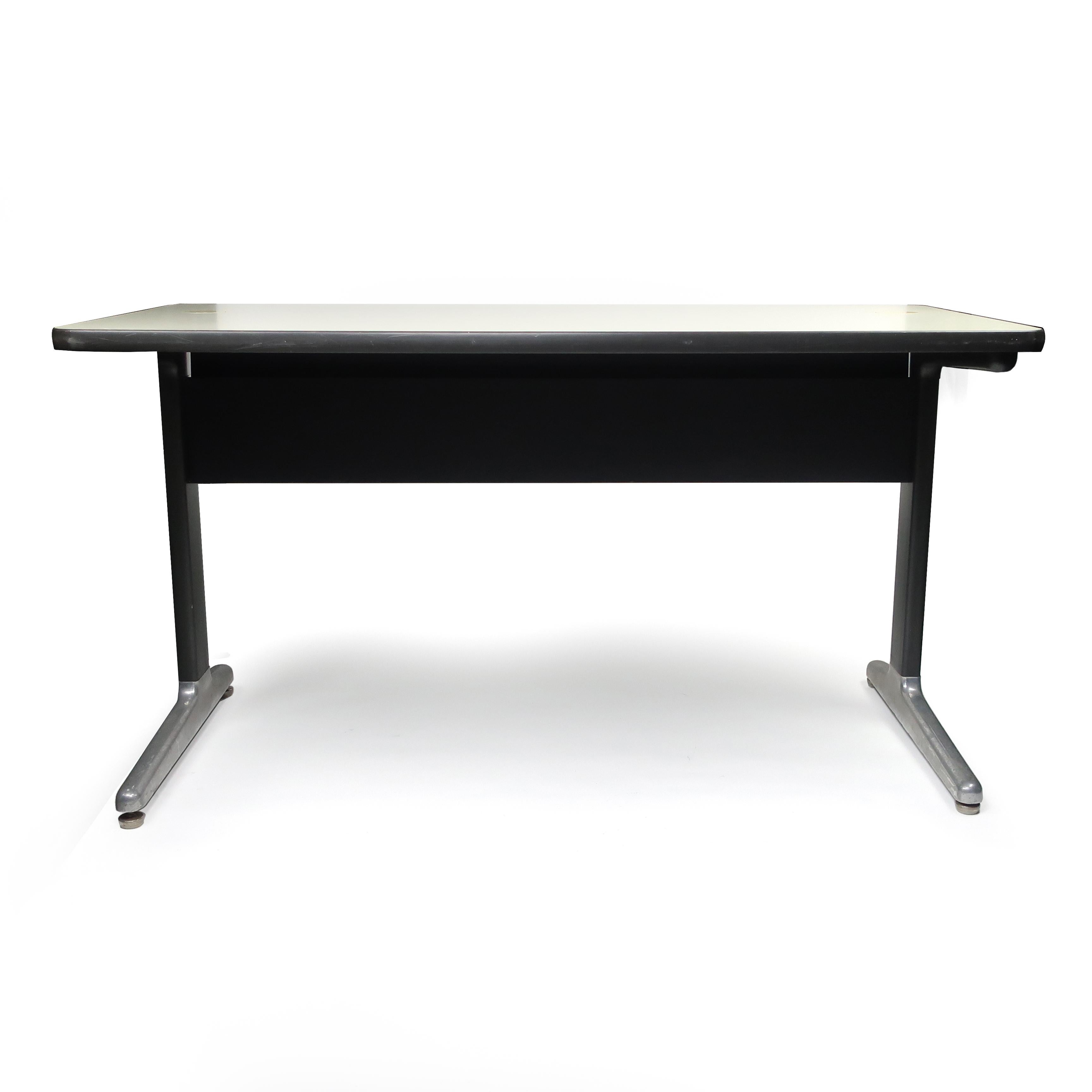 A Classic 1970s Mid-Century Modern desk produced by Herman Miller. Off-white laminate top on black metal base with cast aluminum feet, and includes a black modesty panel and holes to run cables from tabletop devices. Very similar in design to Eames’