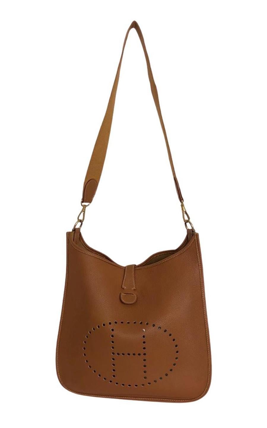Hermès Evelyne GM I (first generation) in cognac colored leather. The hardware is gold-colored. The bag closes with a push button and has no pockets on the inside. It can be worn on the shoulder or as a crossbody bag. The shoulder strap is made of