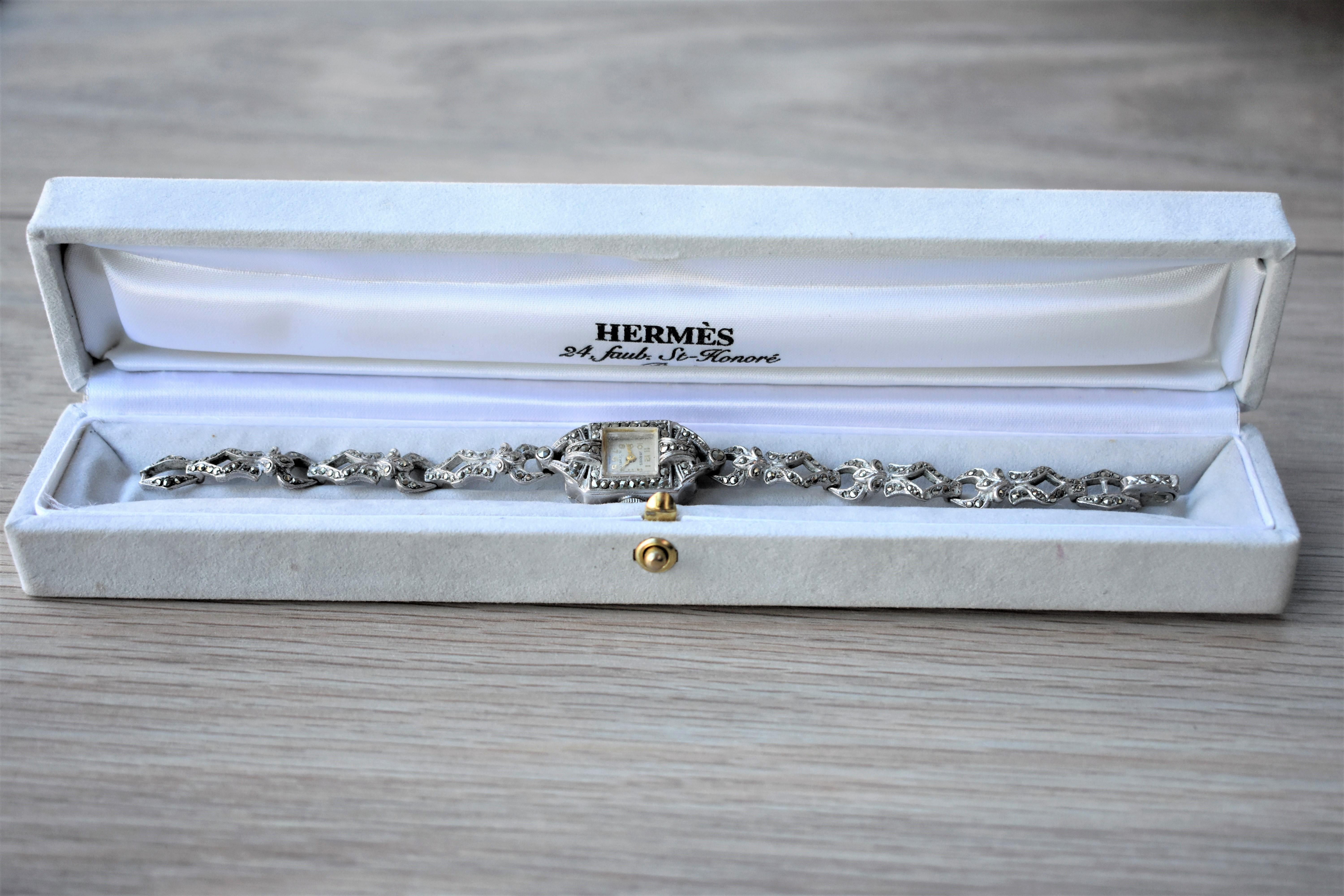 This lovely art deco style cocktail watch by Hermes is made from metal rhodié and decorated with marcasite. It shimmers very classy when light hits the stones. It has a 15 jewel mechanism, currently not working (this is taken into account in the
