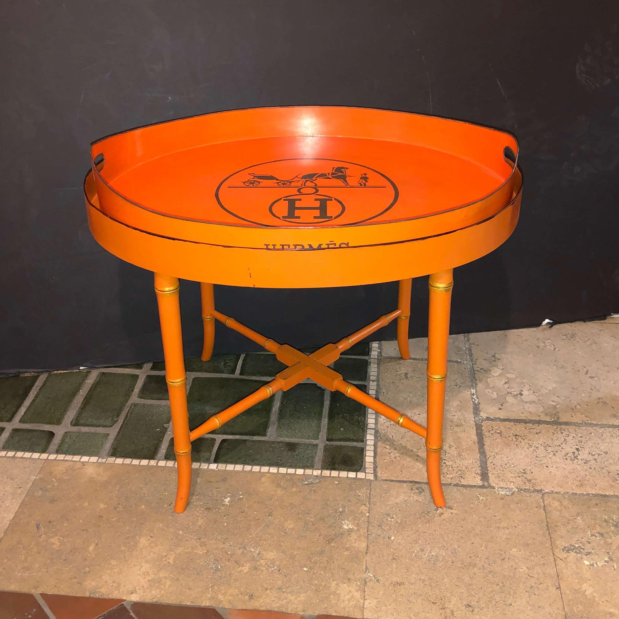 An unusual Hermes orange painted oval tray top cocktail table. The 19th century antique tray, painted Hermes orange and with Hermes logo, on a later faux bamboo base.