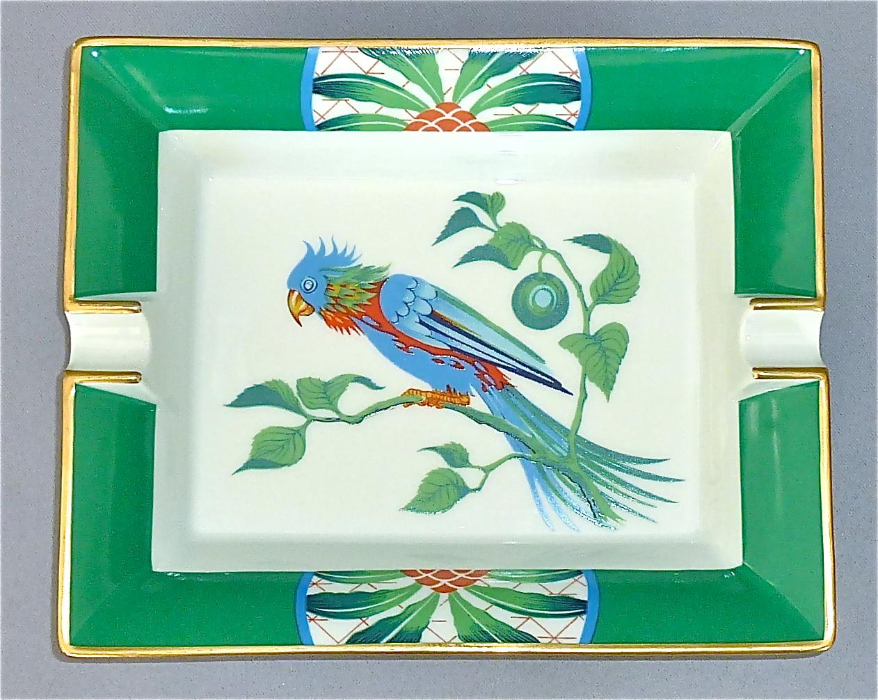 A fine and beautiful Hermès Limoges vintage oblong porcelain ashtray with parakeet bird motif, partly gilt, in colors green, blue and red. Marked Hermes Paris and Made in France to the side and suede covered to the base for protection. This ashtray