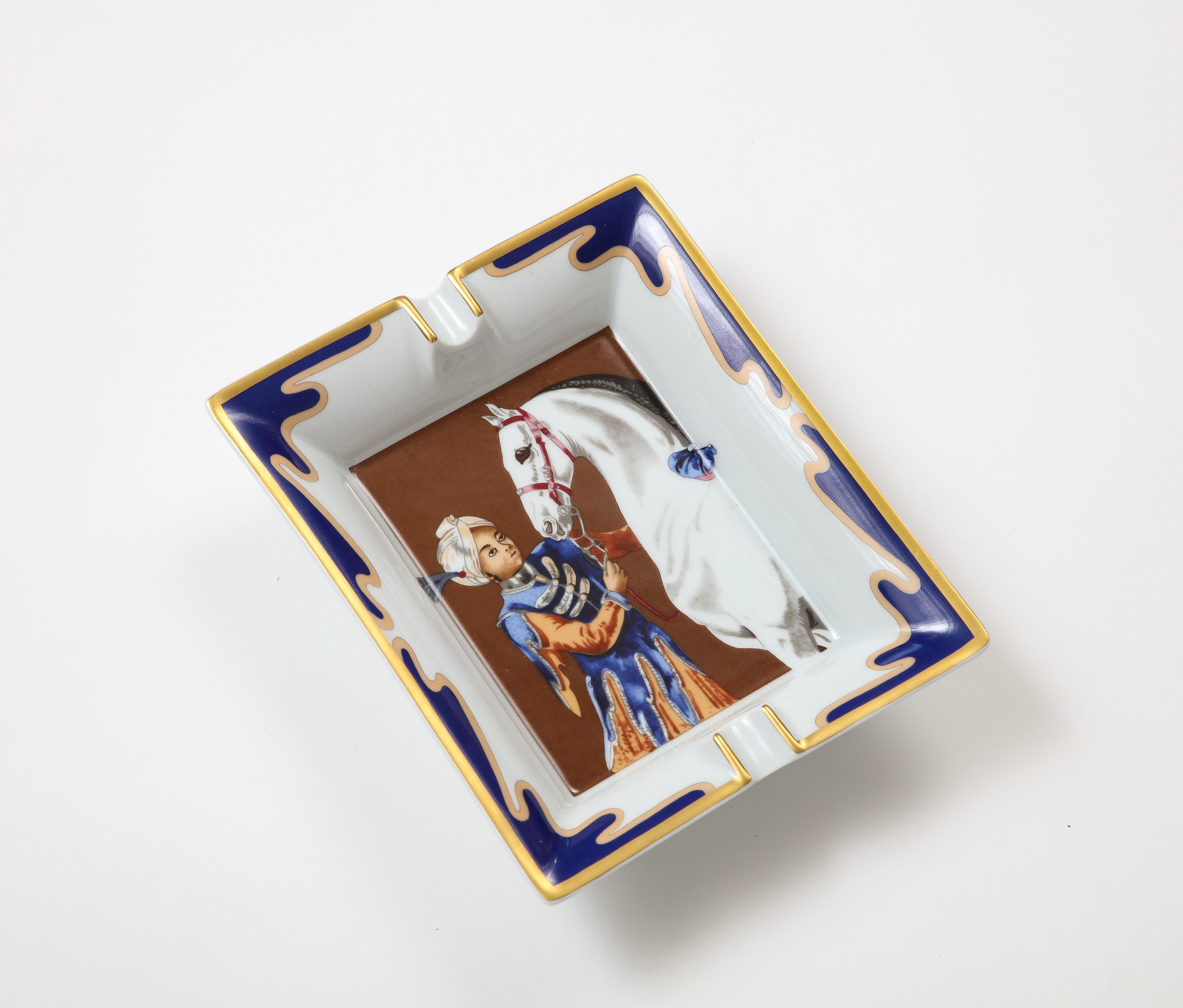 Vintage porcelain ashtray or catchall by Hermes, made in France. The porcelain tray features a man with a horse in the vertical orientation, framed with a lovely blue border with gold trim.
