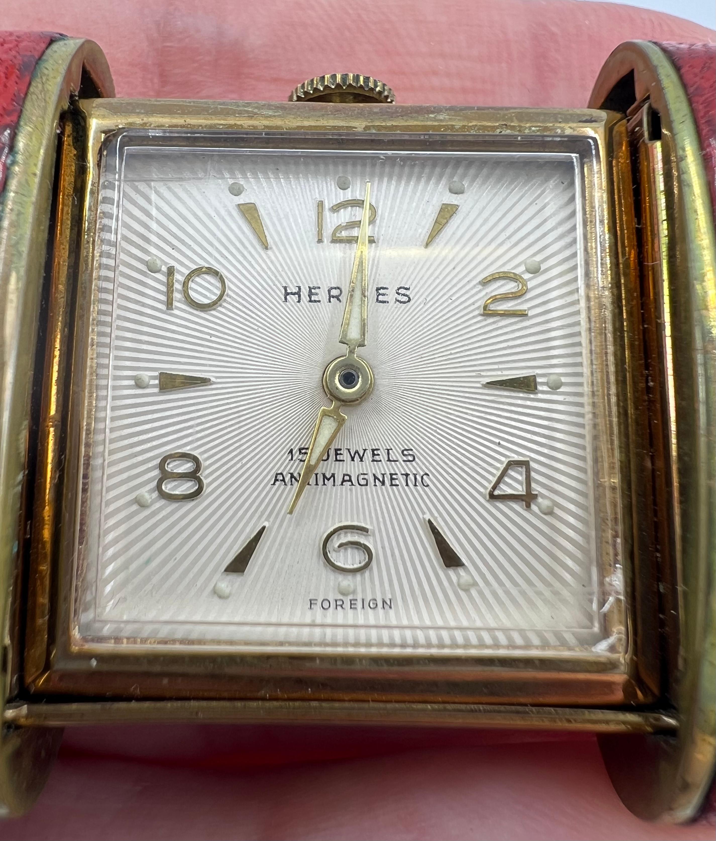 A rare time piece by Hermes, a vintage travel watch. The watch set ina red leather case equipped with a slide opening mechanism.

​The face is square shape, with a white dial and gold alpha shaped hands. Gold Arabic numerals alternate with gold