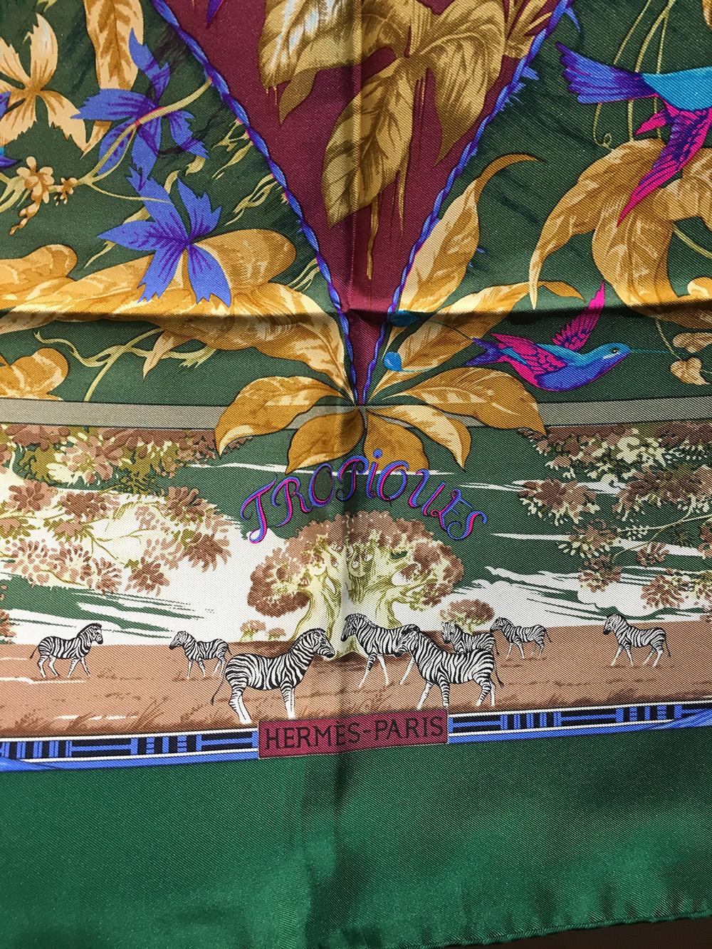 Vintage Hermes Tropiques Silk Scarf in Pink c1980s in good condition. Original silk screen design c1987 by Laurence Bourthoumieux features various tropical flora and fauna over a forest green background. Zebras and giraffes in palm desert scenes