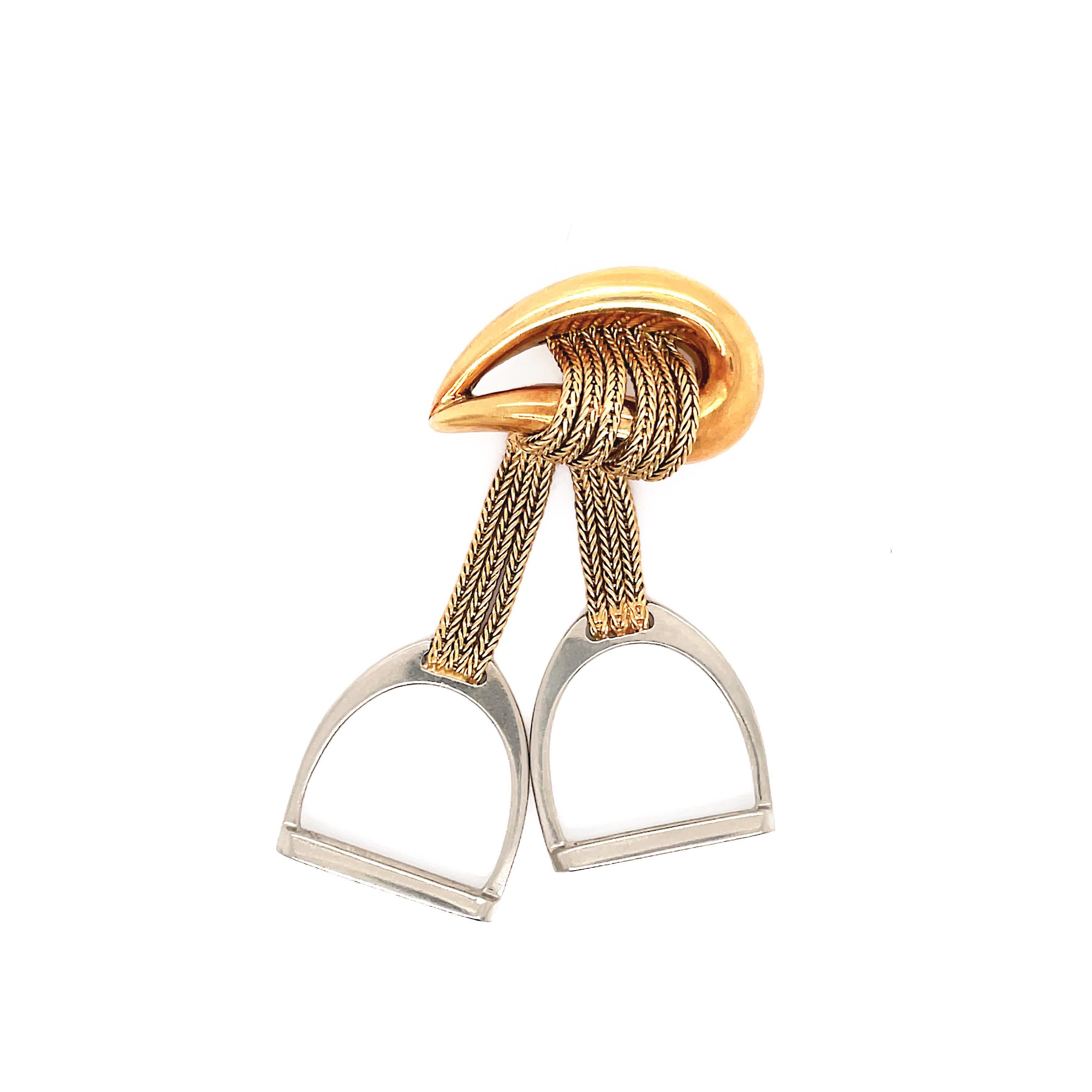 This rare vintage 18 carat gold HERMES brooch is a signature style of the French brands' equestrian design aesthetic. Hanging from a teardrop shaped brooch are two strands of yellow gold chain holding onto two solid white gold stirrups. The piece is