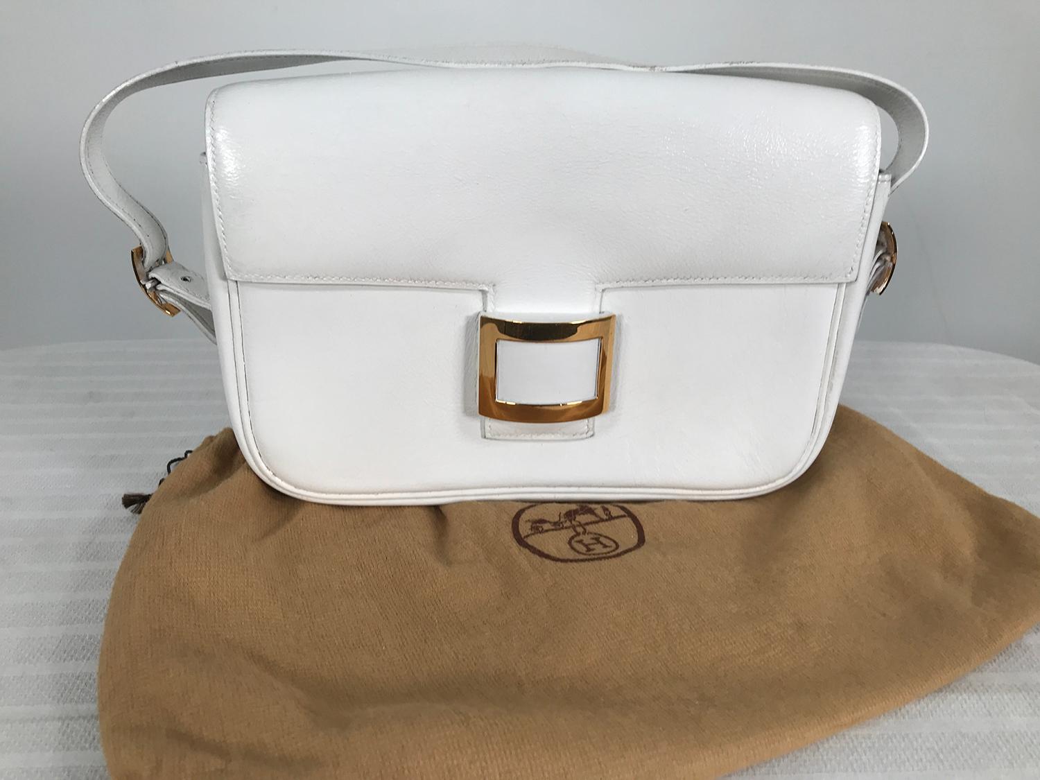 Vintage Hermes white flap front bag with gold buckle front and center front tab closure. Short handle or strap, with gold buckles at either bag side. From the 1980s M in a circle date code stamped on the leather zipper pull tab inside the bag. The