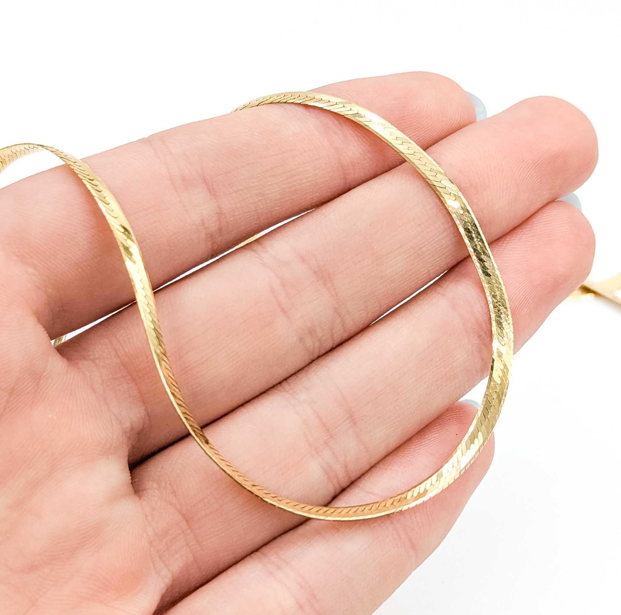 This sleek vintage herringbone necklace is crafted in 14k yellow gold and measures 30 inches in length with a 2.7mm width. Its fluid, flat-link design lies gracefully against the neckline, reflecting light with every movement for a sophisticated,