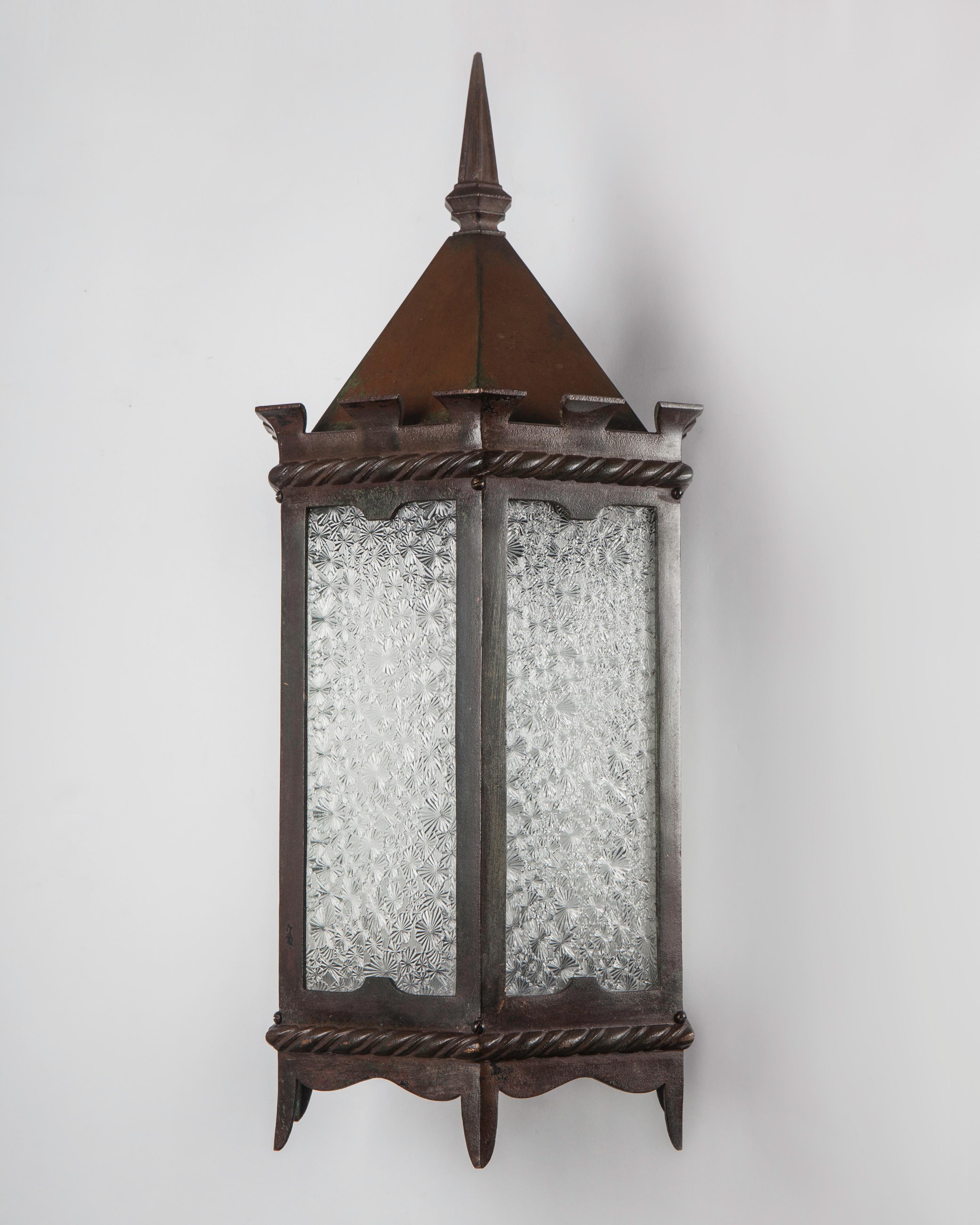 AEX0599
Circa 1920
A pair of vintage bronze exterior wall lanterns with hexagonal bodies glazed with frosted, textured glass. The twin backplates in the form of leafy quatrefoils. In their original age-worn mottled finish, the red hue including