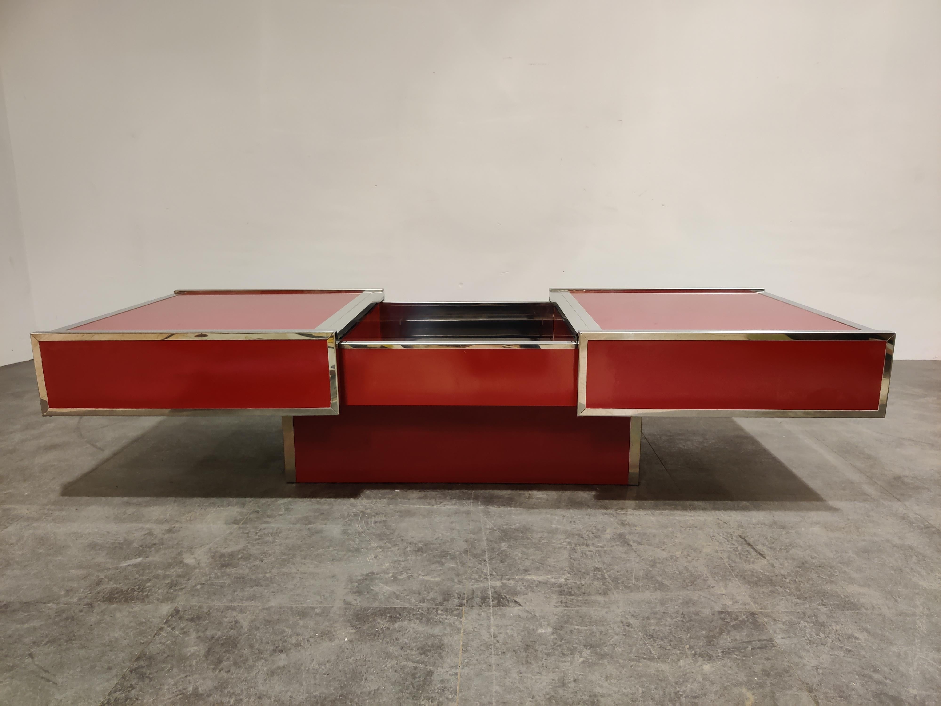 Eye catching red lacquered metal and chrome hidden bar coffee table.

The tables tops slide open to reveal a chromed bar compartment.

Very much in the style of Willy Rizzo.

Rare piece to find in a bright red colour.

Good condition, small