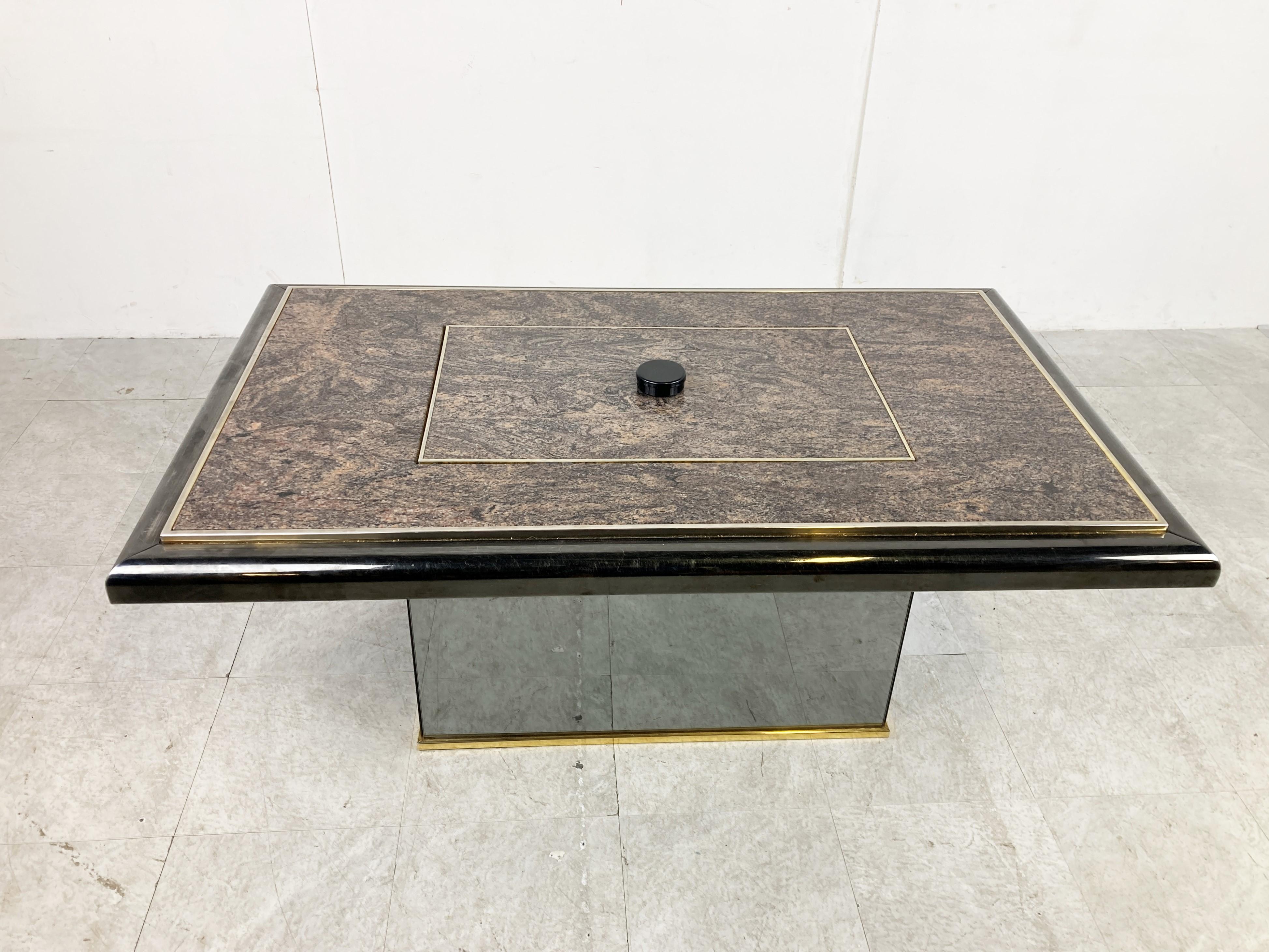 Unique coffee table that, with a twist of the knob, reveals a hidden bar compartment.

The coffee has a brass and mirrored glass base with a granite and lacquered wooden top.

Very good condition

1980s - Belgium

Dimensions: 
Height: