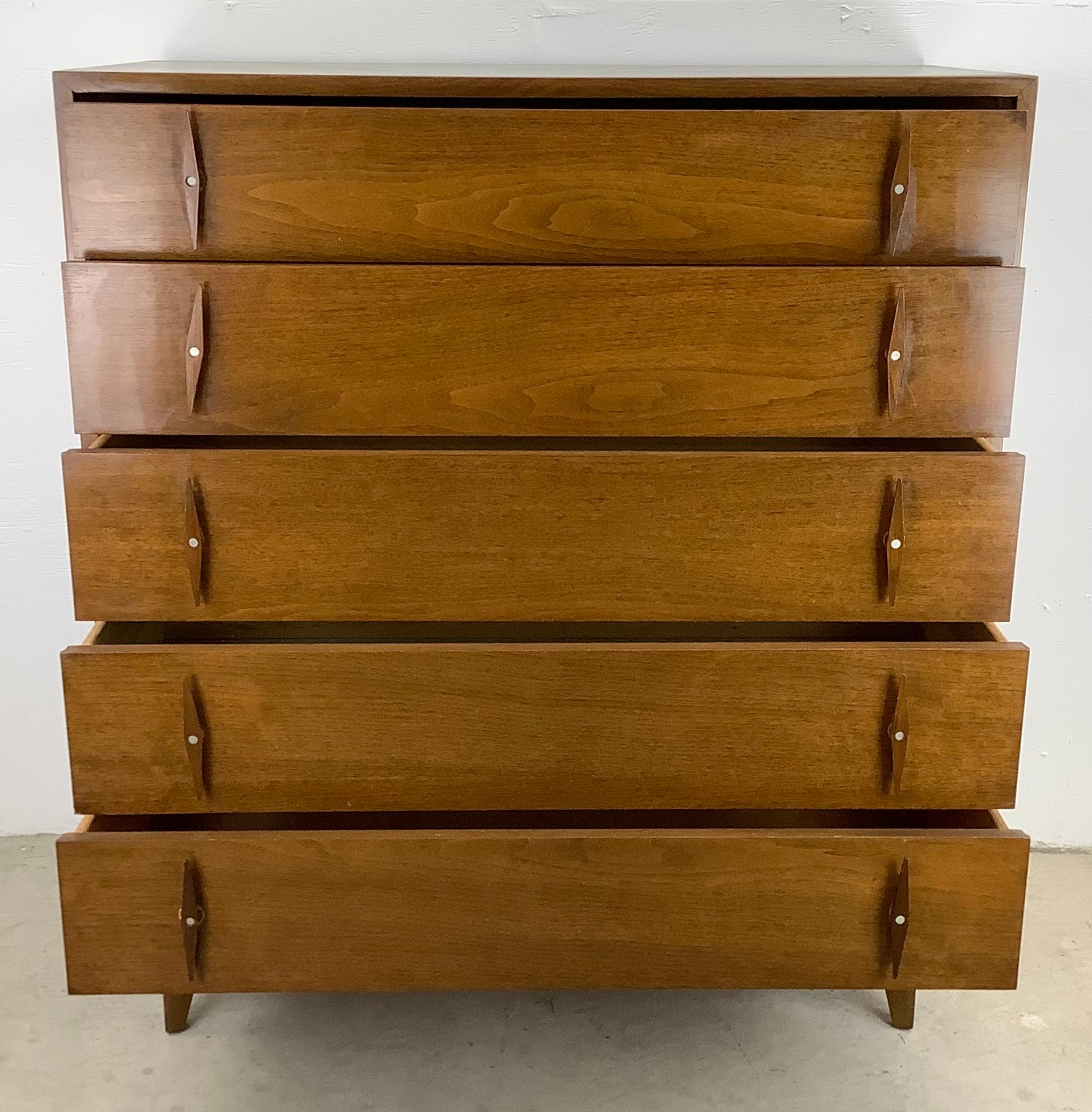 This striking vintage walnut five drawer Highboy Dresser from American of Martinsville is a captivating and functional piece that brings mid-century charm to your bedroom decor. With its striking carved wood pointed handles, this dresser adds a high