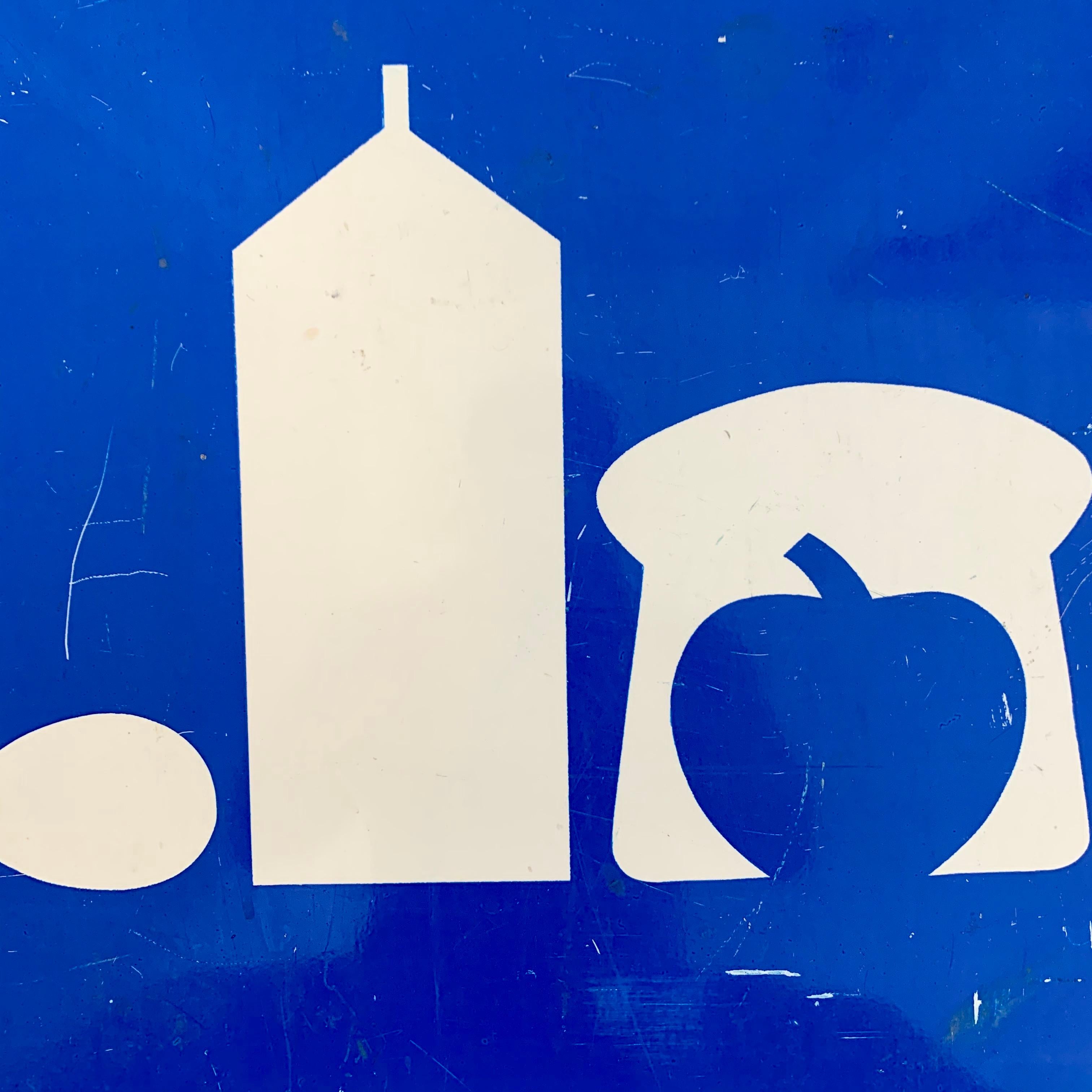 Rare blue and white metal sign taken down from a US highway. Sign shows images of an egg, carton of milk, bread and an apple. Sign was used to show drivers that there is a market ahead. Sign is 2 feet by 2 feet. Cool piece of transportation history.