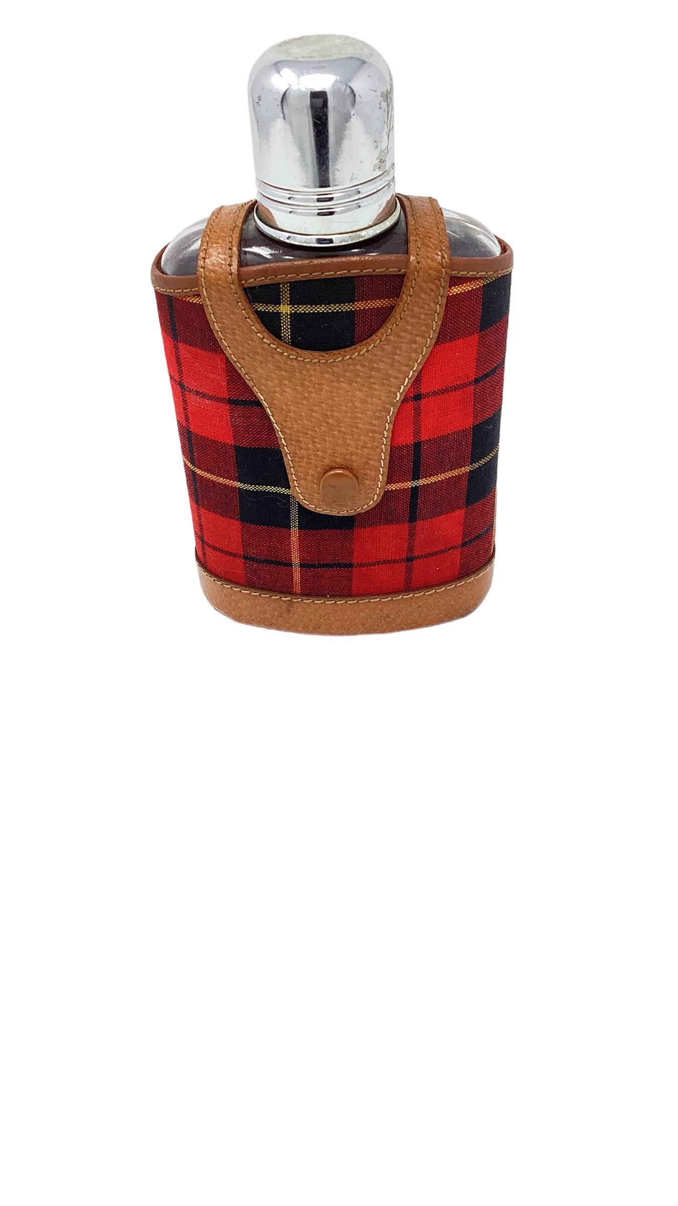 Flasque vintage avec couvercle en cuir et en tissu écossais. Un écossais aux couleurs vives et du cuir de porc souple cousu à la main entourent la gourde en verre.