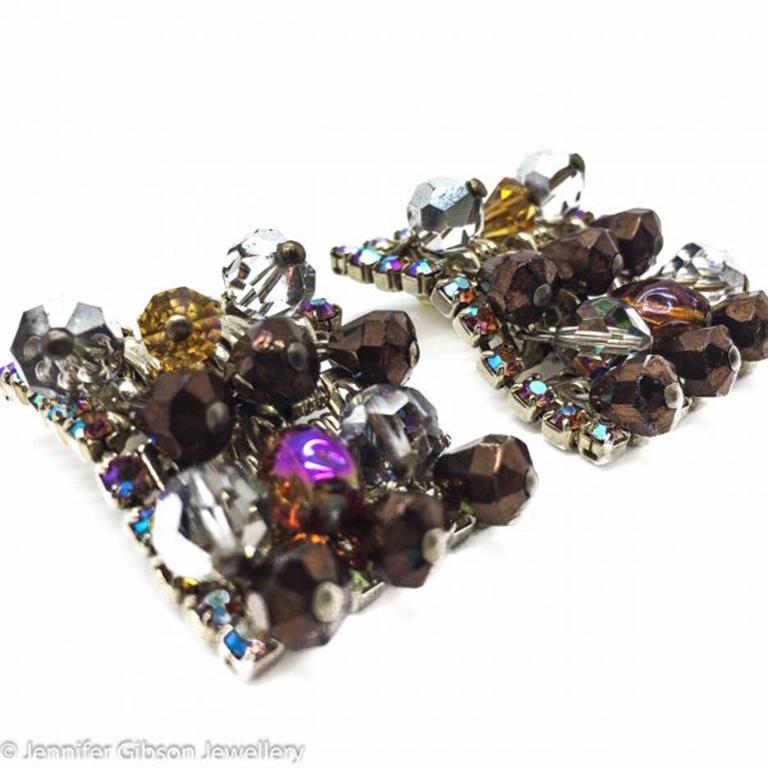 Un fabuloso par de pendientes Hobe Vintage súper glamurosos de mediados de siglo. Pinzas articuladas rectangulares, totalmente cargadas, que gotean cristales de abalorios en gloriosos tonos de marrón metálico, gris y ámbar. Un acabado de aurora