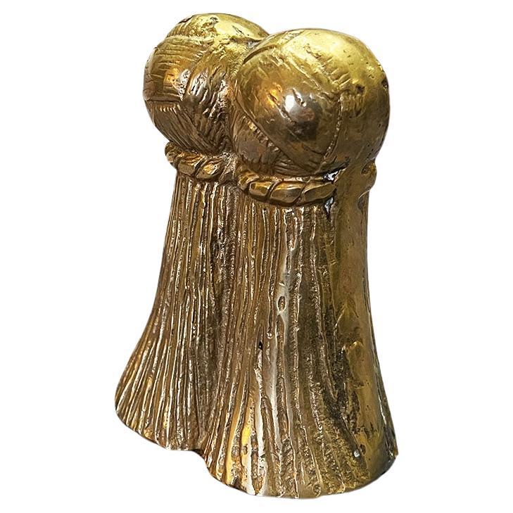 A Hollywood Regency brass tassel motif bookend. Created from heavy brass, this piece will be a wonderful way to hold up your favorite books on a bookshelf in a beautiful way. The piece depicts two large faux tassels with round balls on top. The back