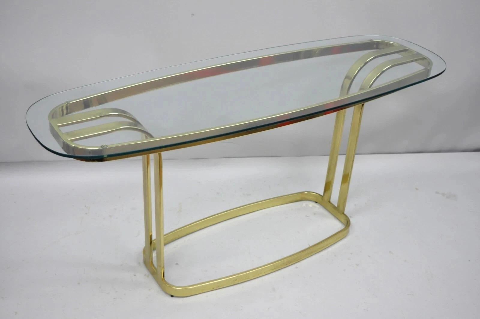 Vintage Hollywood Regency Brass and Glass Sculptural Console Sofa Table. Item features a shaped glass top, sculptural brass base, and clean Modernist lines. Circa Late 20th Century. Measurements: 26