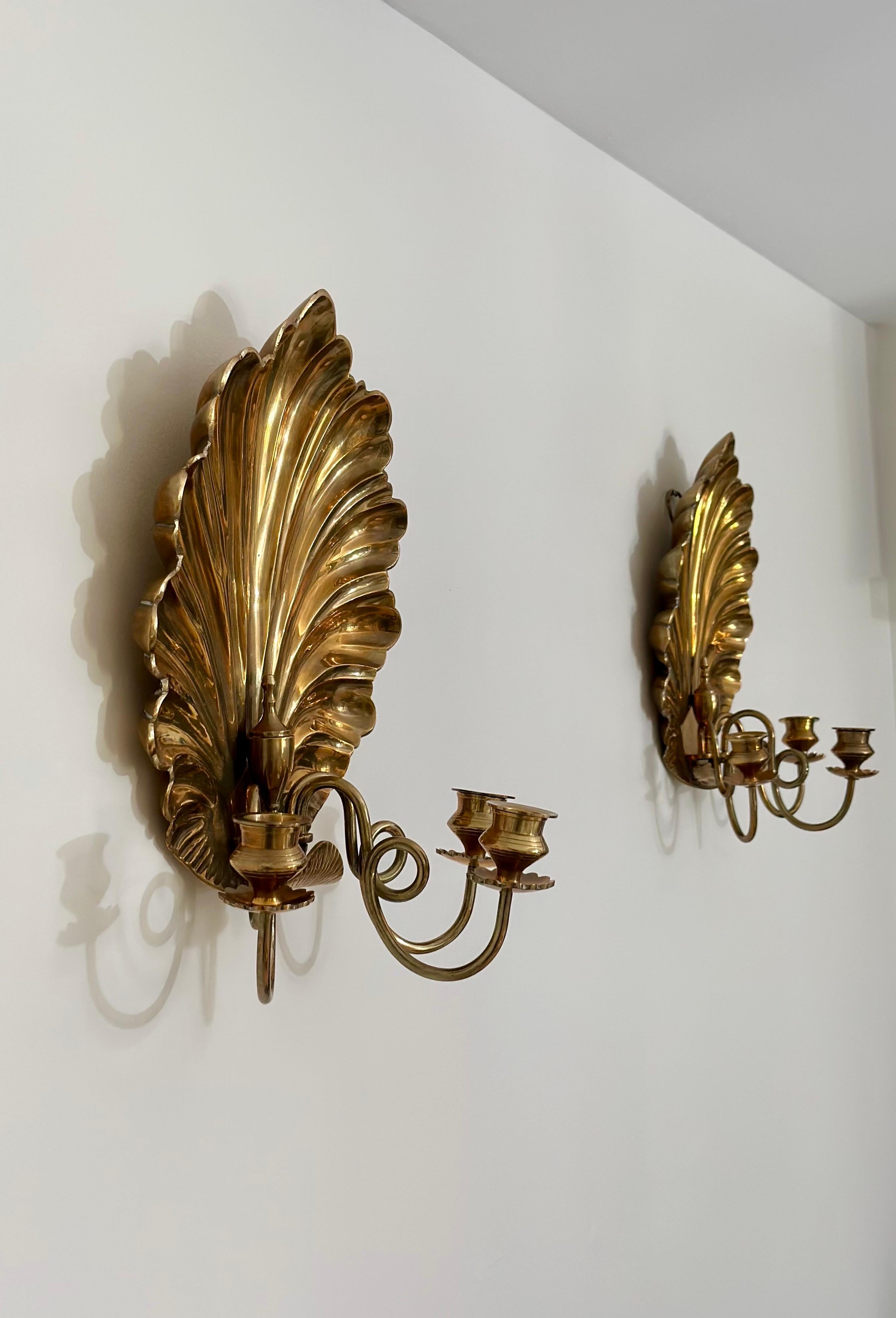We are very pleased to offer a striking pair of vintage brass wall sconces, circa the 1980s.  This pair features bold, sculptural shell-shaped backplates with a radiant, brass finish that catches the light beautifully.  Designed in a dramatic shell