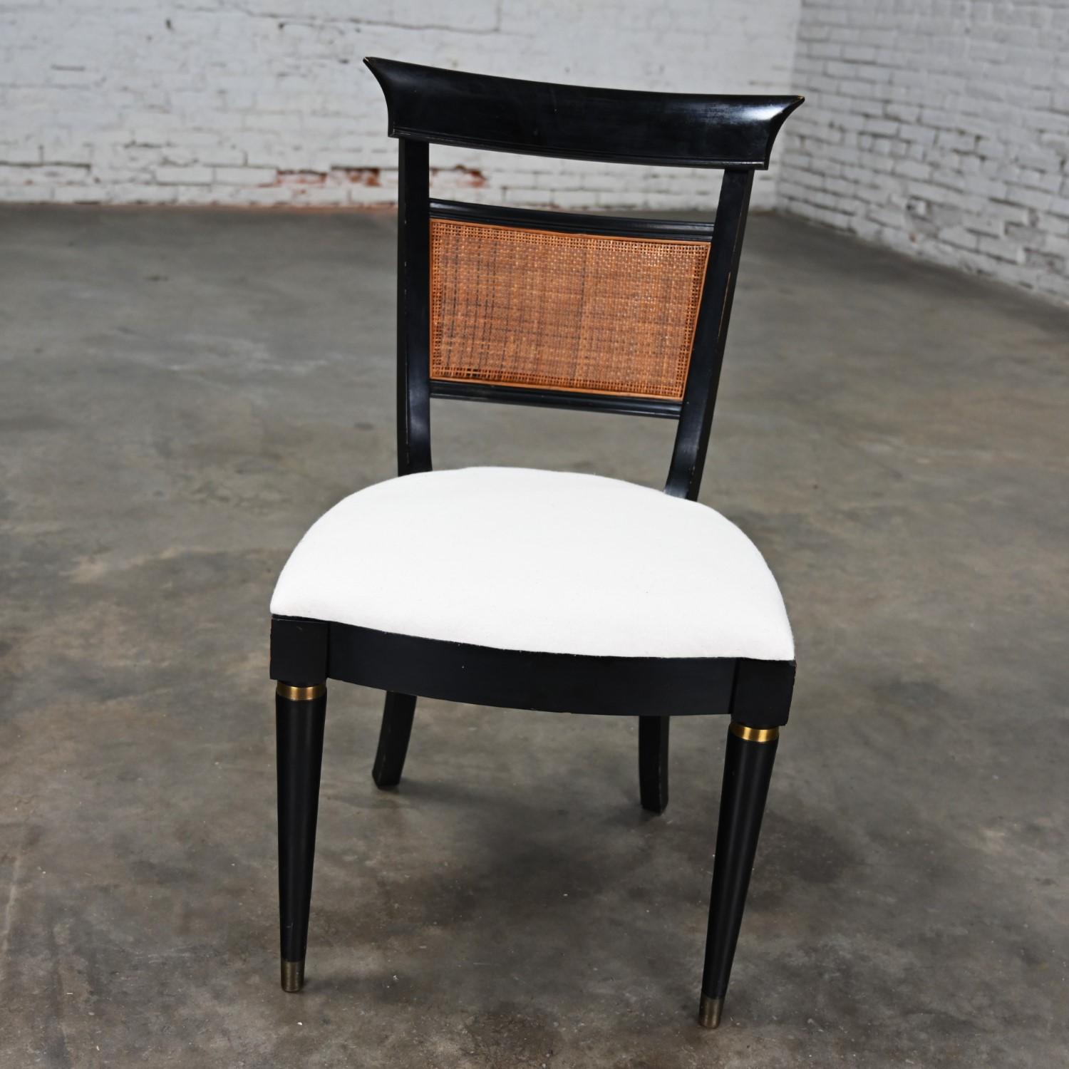 Stunning Mid-20th Century distressed Hollywood Regency Charlotte Chair Company accent chair with black painted wood frame, radial weave natural cane back inset, off-white canvas seat, brass ring upper leg details, and front brass sabots.  Beautiful