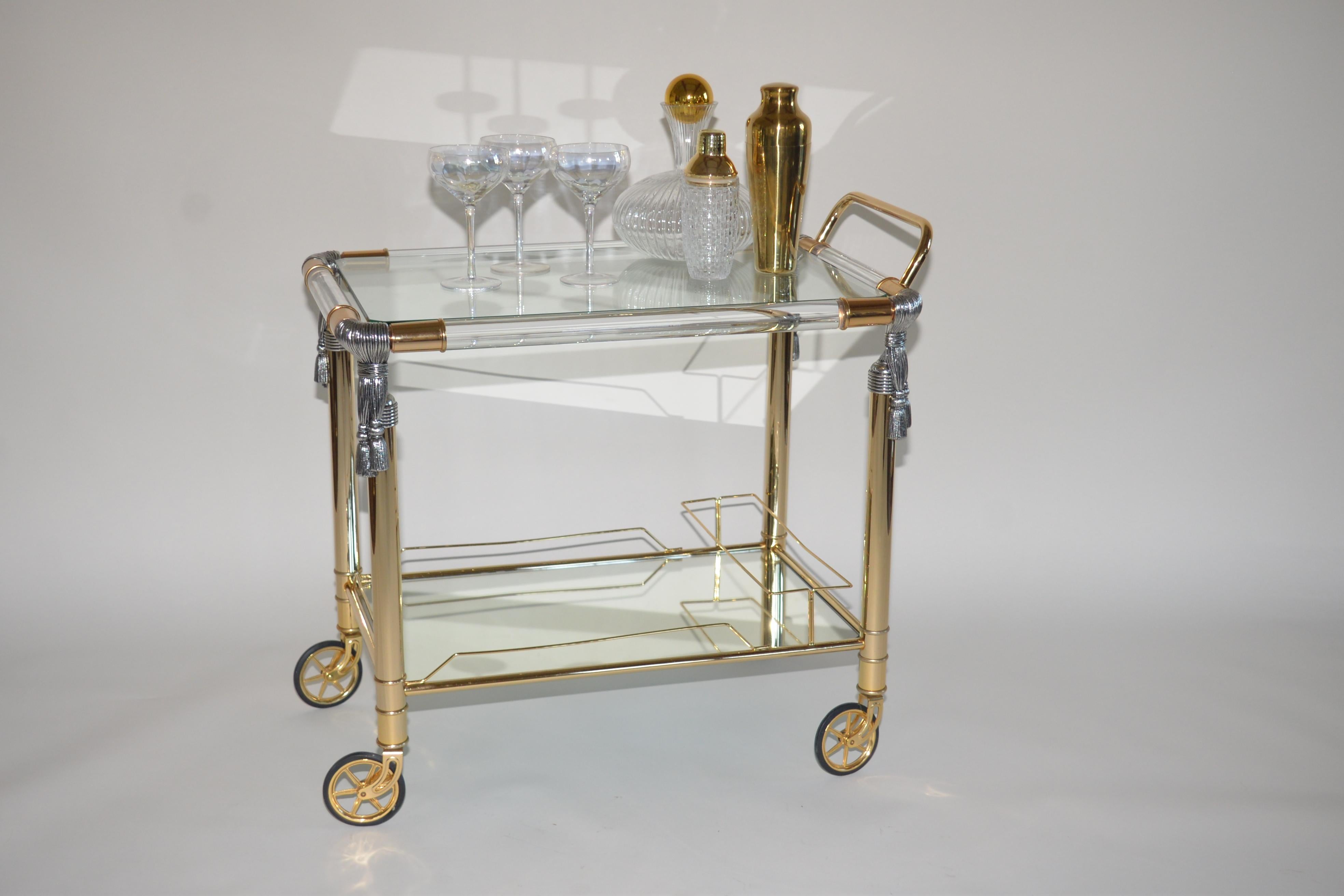 A gorgeous Hollywood Regency style vintage drinks trolley by Curvasa Meubles. Lucite and gold with silver rope detailing on each corner. Two shelves with the lower shelf being mirrored glass. A very striking item.
