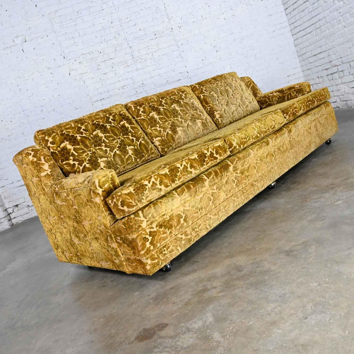 Gorgeous vintage Hollywood Regency style greenish-gold colored floral cut velvet modified Lawson style sofa with loose seat and back cushions, three casters in front, and two round tapered wood legs in the back. Beautiful condition, keeping in mind