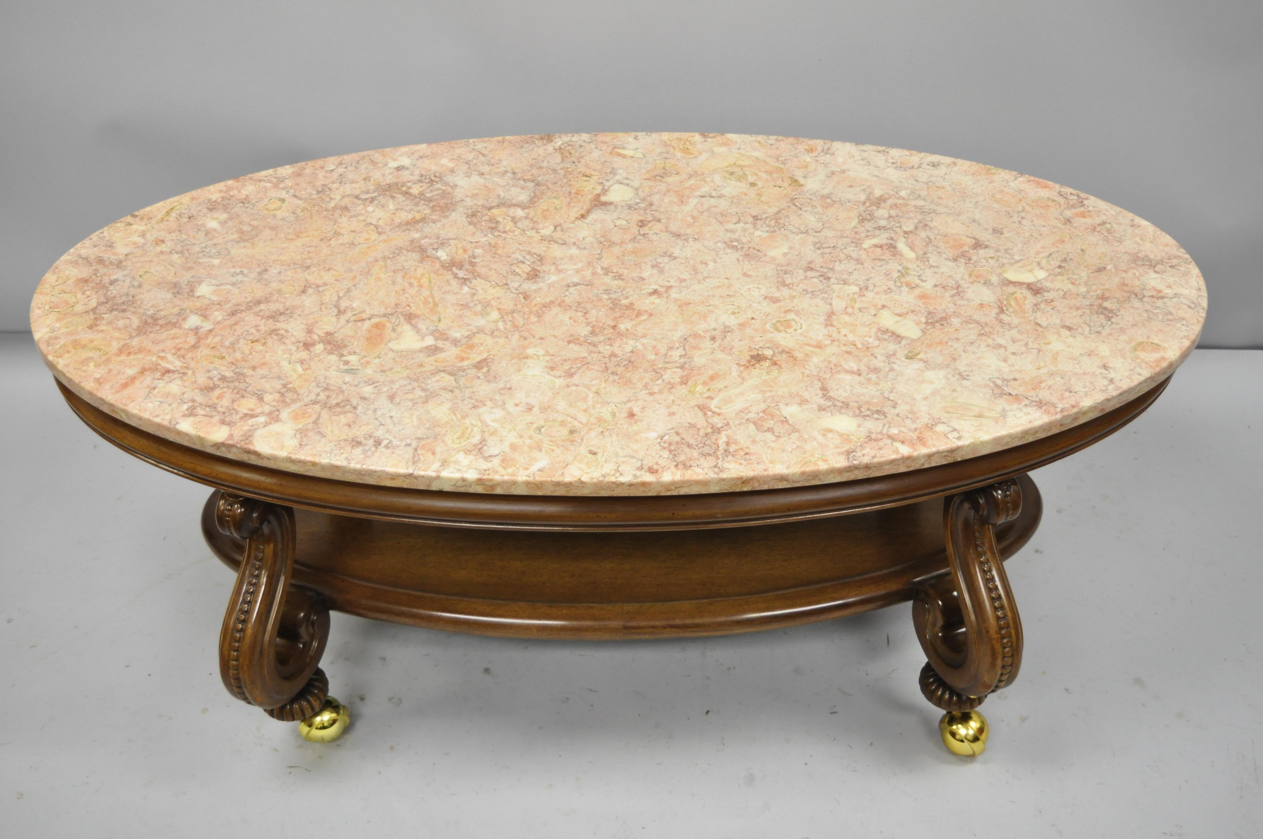 Vintage Hollywood Regency French style pink marble-top oval coffee table. Item features solid mahogany base, lower shelf, rolling casters, pink marble top, nicely carved details, great style and form, circa 1950. Measurements: 20.5