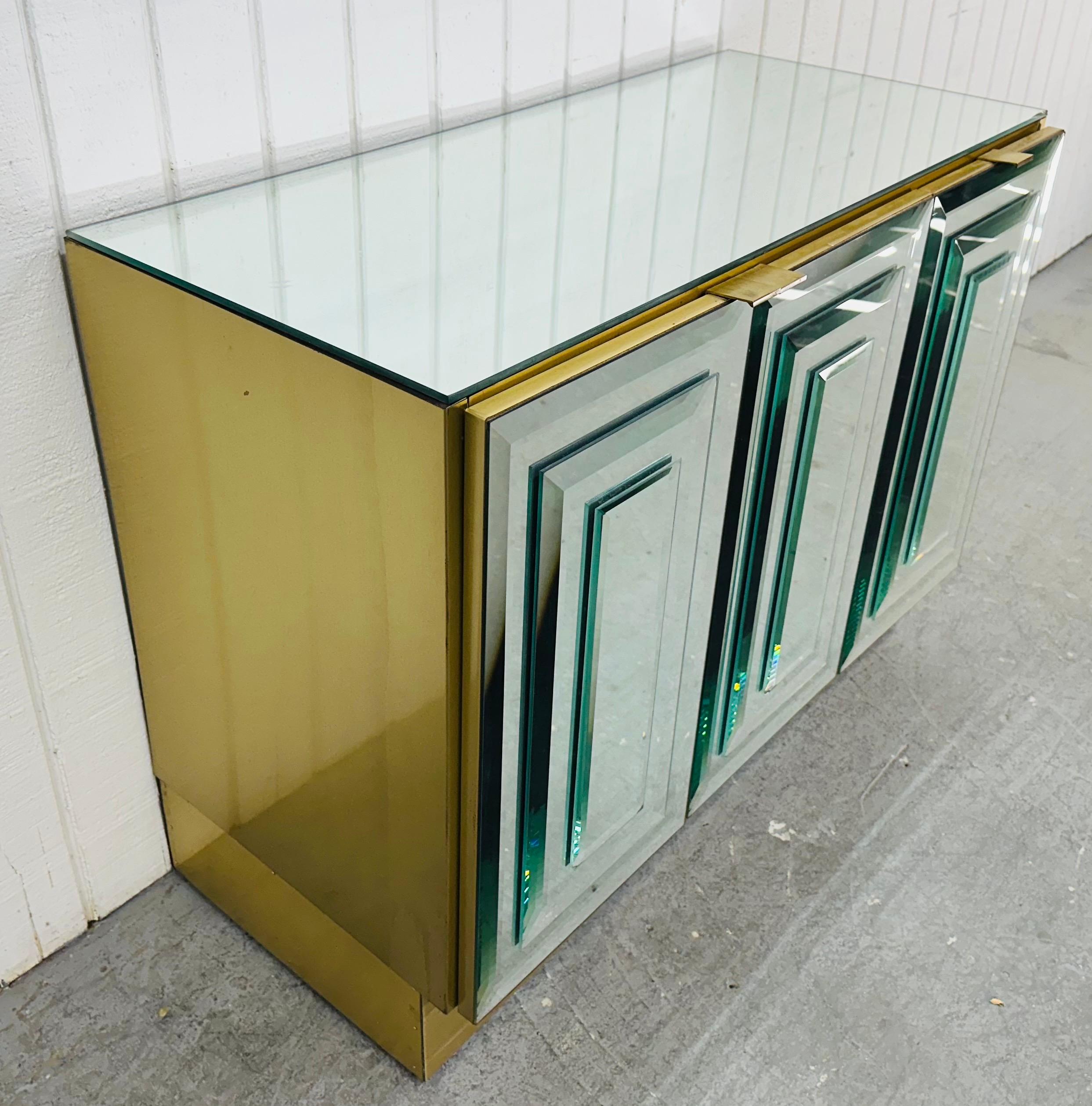 This listing is for a Vintage Hollywood Regency Mirrored Storage Cabinet. Featuring a straight line design, three mirrored doors that open up to storage space, mirrored top, brass sides and plinth base. This is an exceptional combination of quality